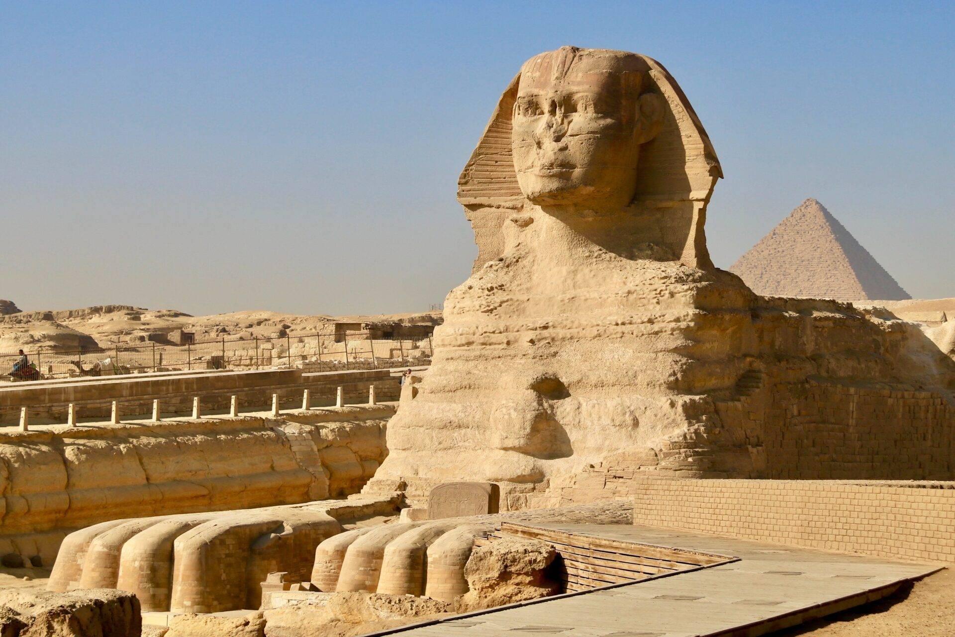 The Great Sphinx of Giza facing a pyramid, with architectural remains and protective barriers in the foreground