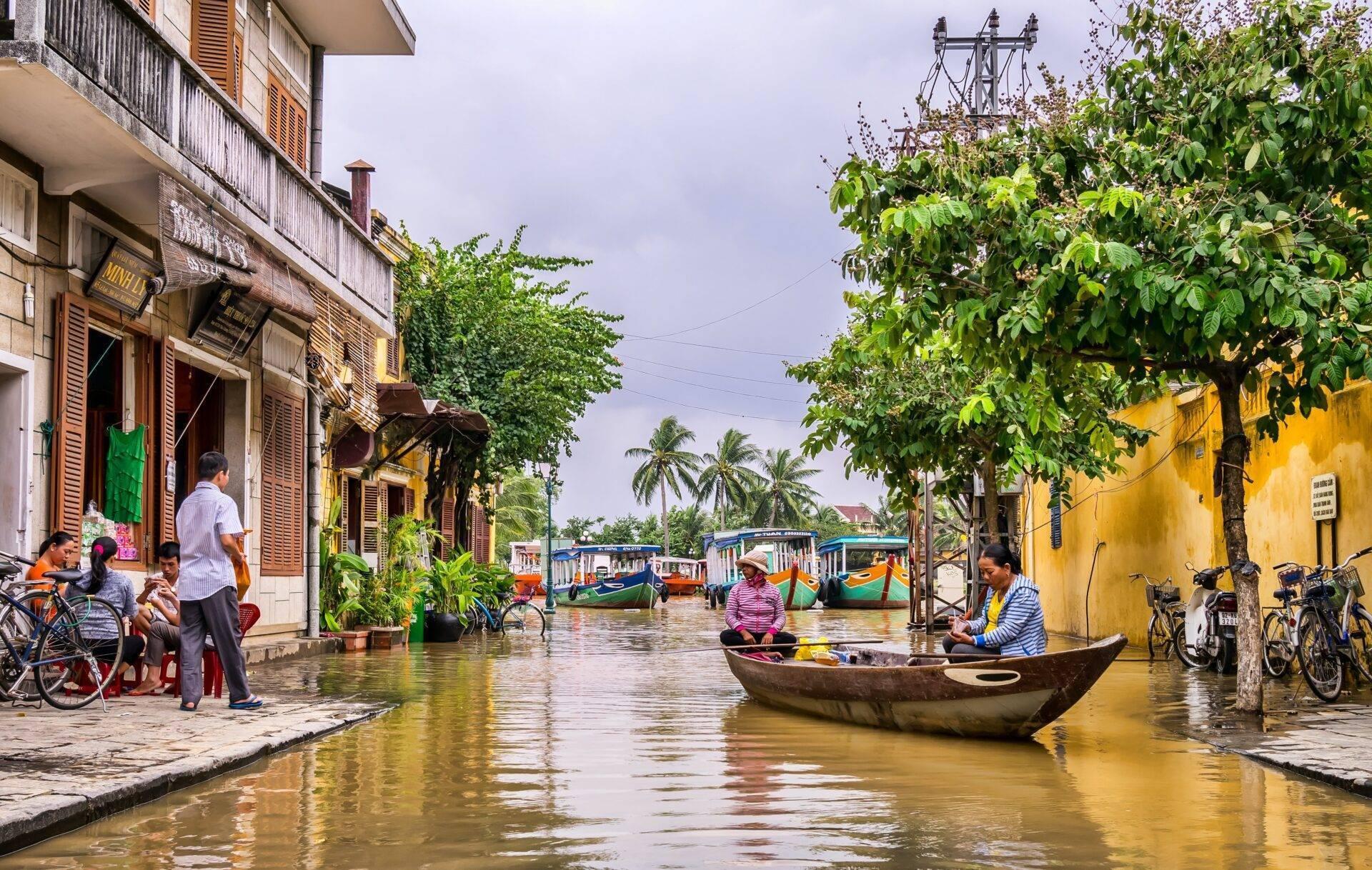 Une rue inondée d’une ville vietnamienne avec des bateaux, des maisons colorées et des habitants circulant en vélo