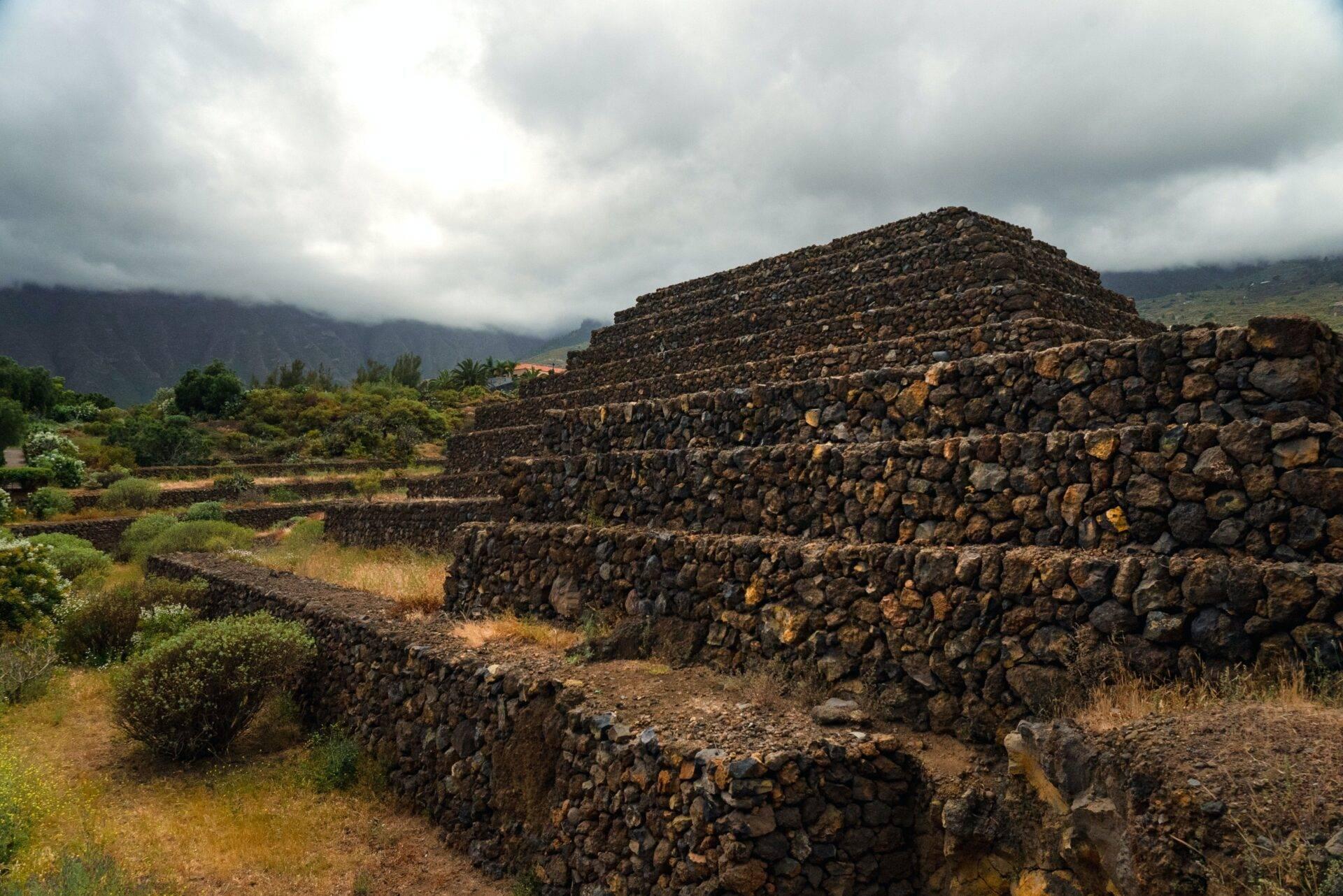 Ruines de pierre empilées dans un paysage volcanique avec montagnes brumeux et végétation méditerranéenne aux Canaries