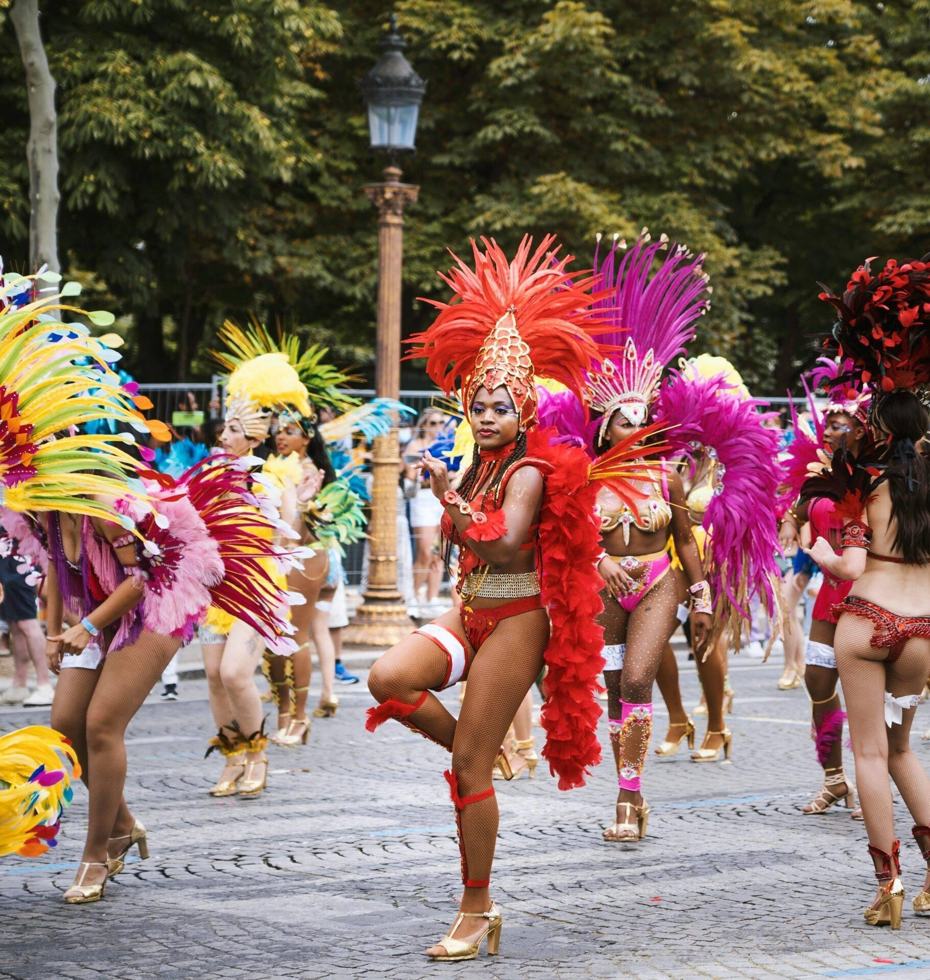 Défilé de carnaval avec danseuses en costumes colorés et plumes, rue pavée, lampadaire en arrière-plan