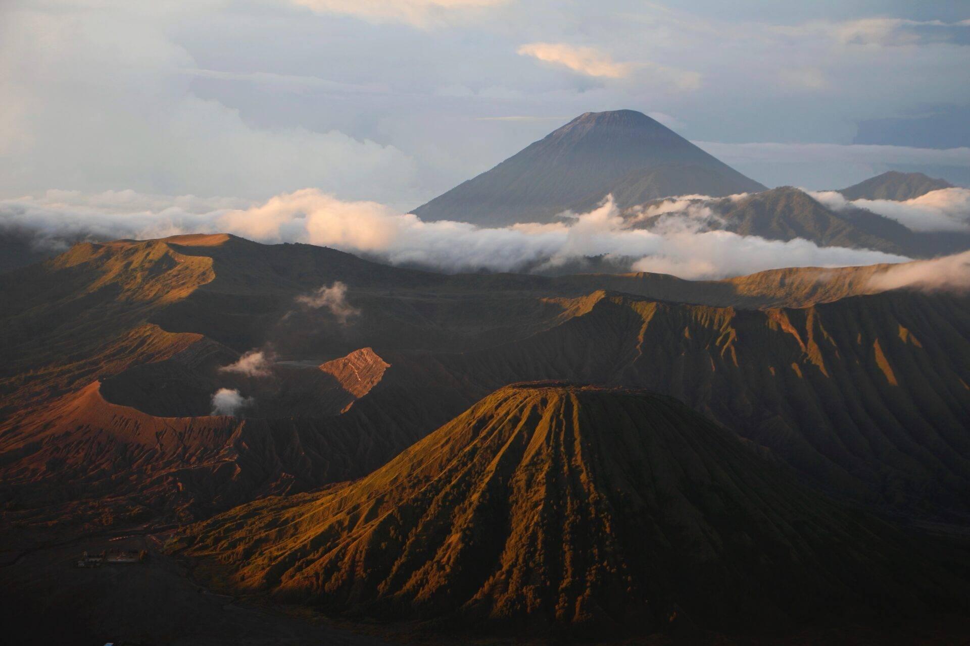 Vue aérienne de volcans avec cratères et pentes striées sous lumière dorée, brumes basses entre les pics