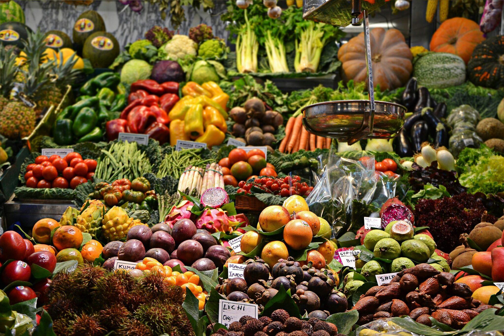 Un étal de marché coloré présentant fruits, légumes exotiques et produits frais avec eau versée en continu