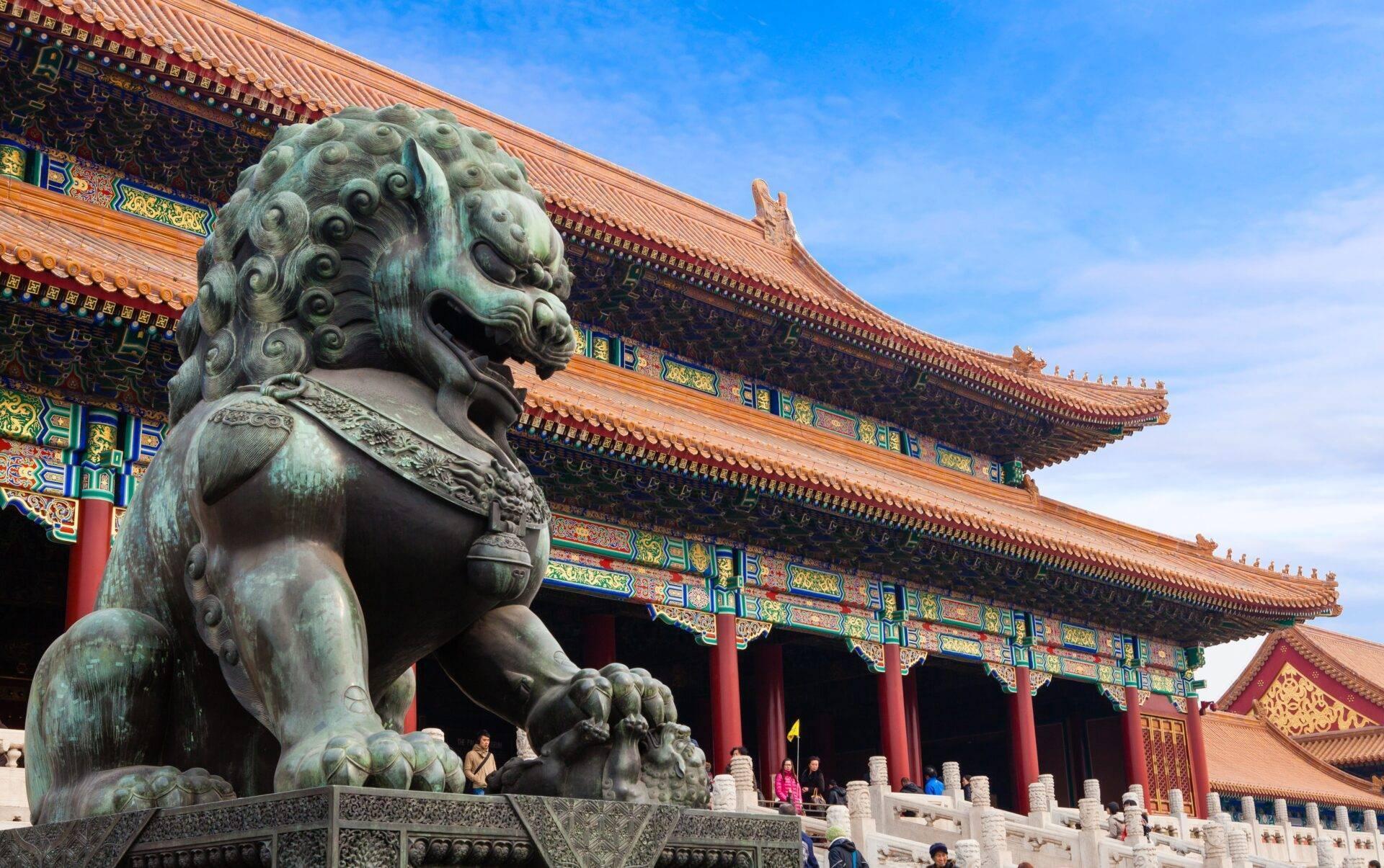 Un lion de jade vert en garde devant un temple chinois aux toits dorés ornés et colonnes rouges