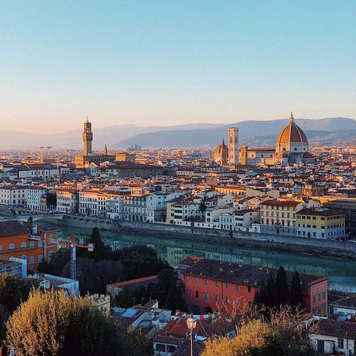 Vue panoramique d’une ville historique avec cathédrale à dôme doré, fleuve et montagnes en arrière-plan au coucher du soleil