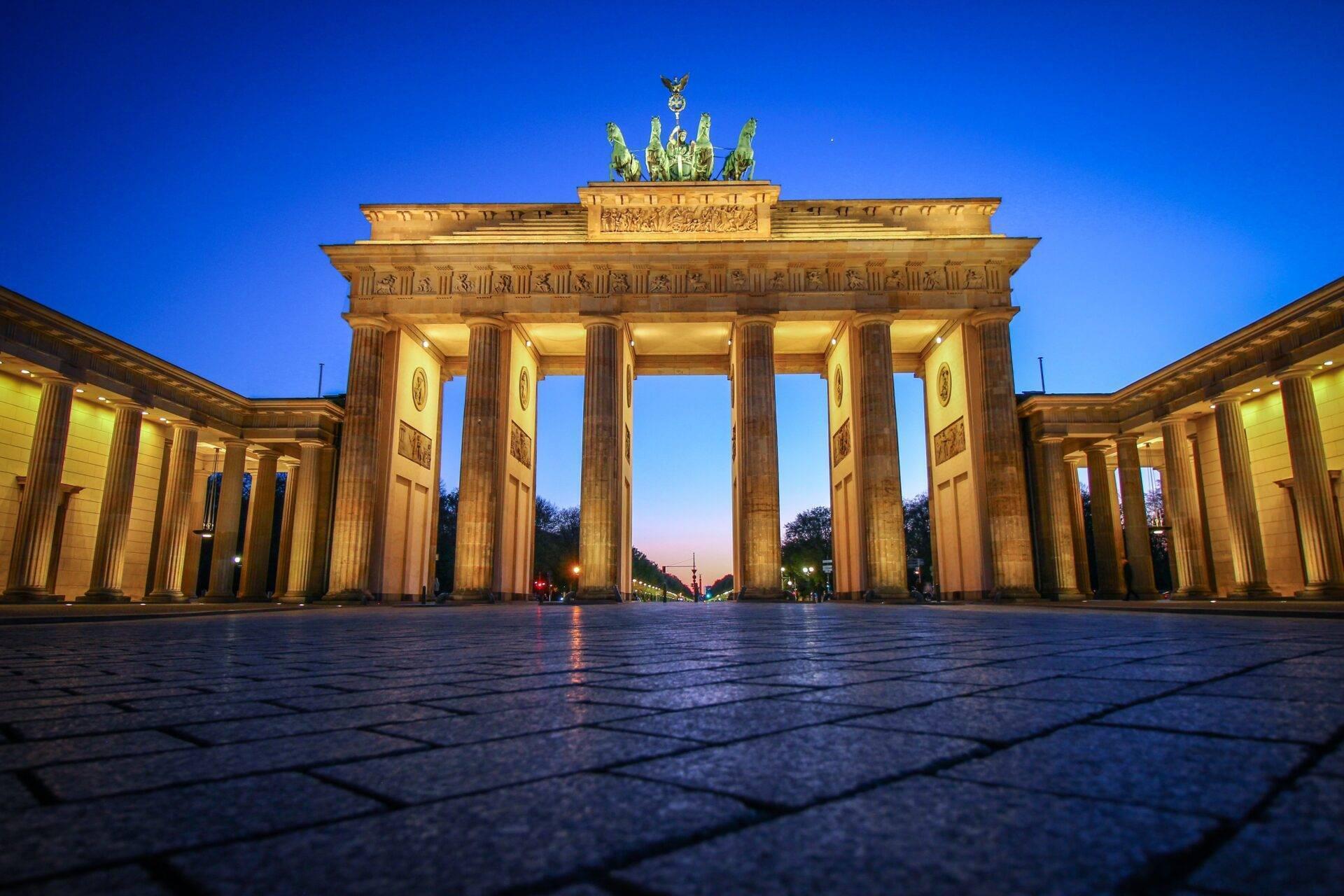 Imposing historic monument with gilded columns illuminated at dusk, crowned by a golden quadriga
