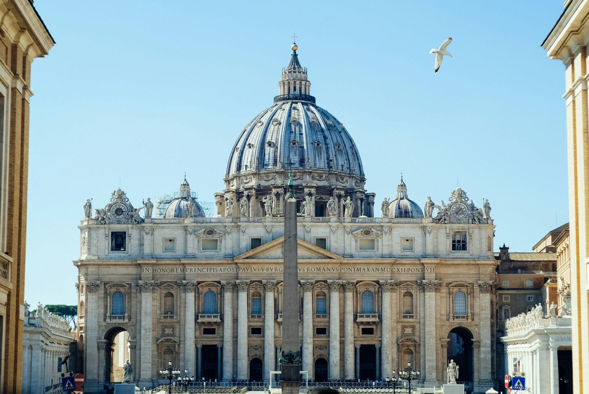 Grand basilica with a central Renaissance dome, colonnade and obelisk under a clear sky