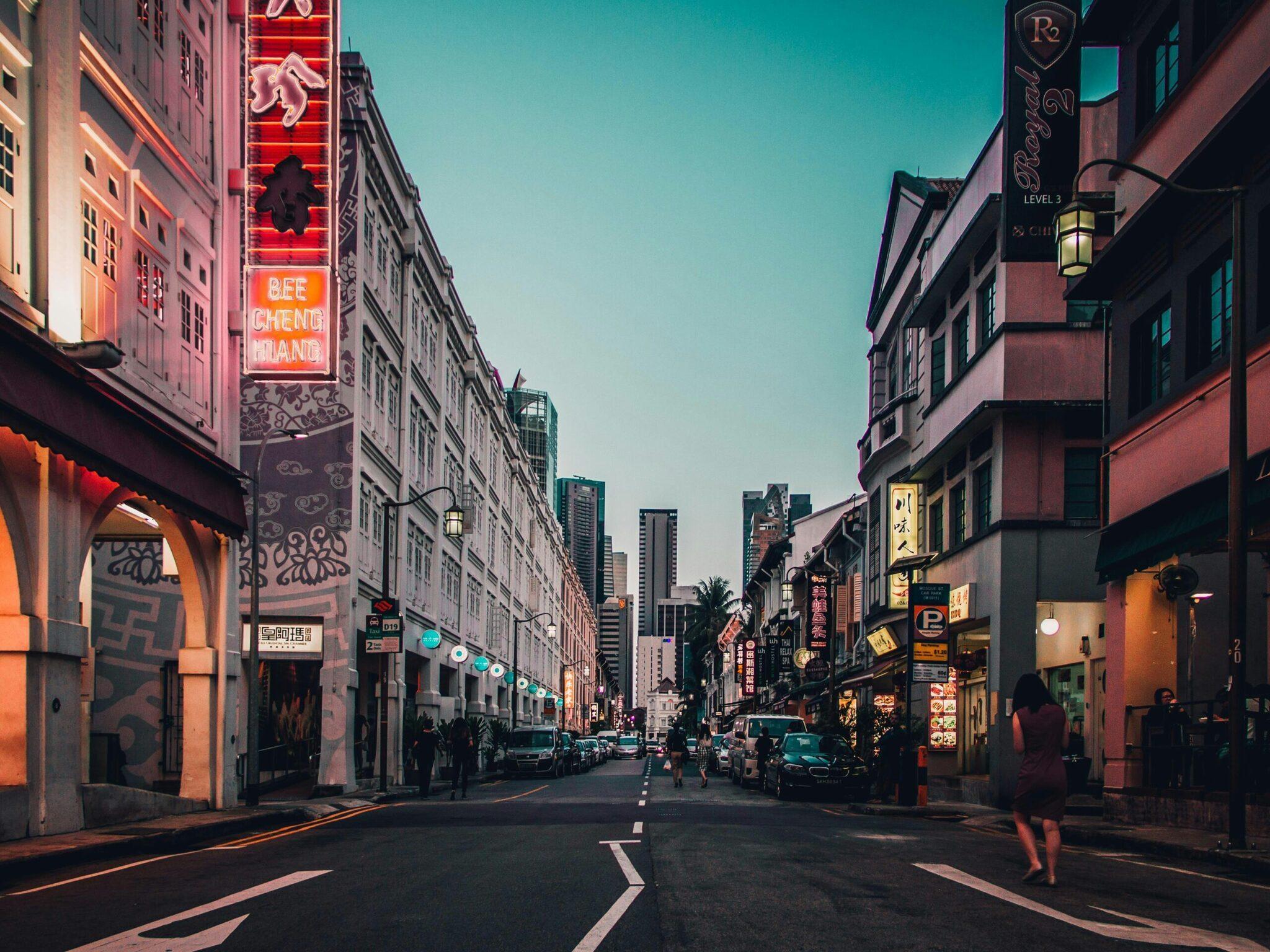 Une rue commerçante asiatique illuminée de néons rouges avec immeubles historiques et gratte-ciel en arrière-plan au crépuscule