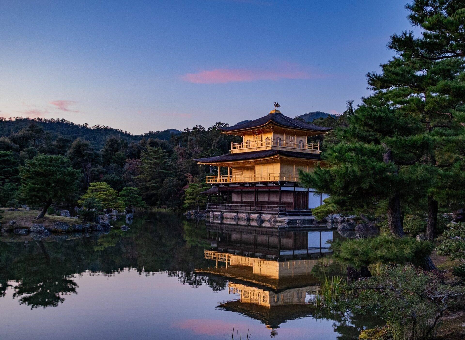 A two-storey golden pavilion reflected in a calm lake surrounded by lush forest at dusk