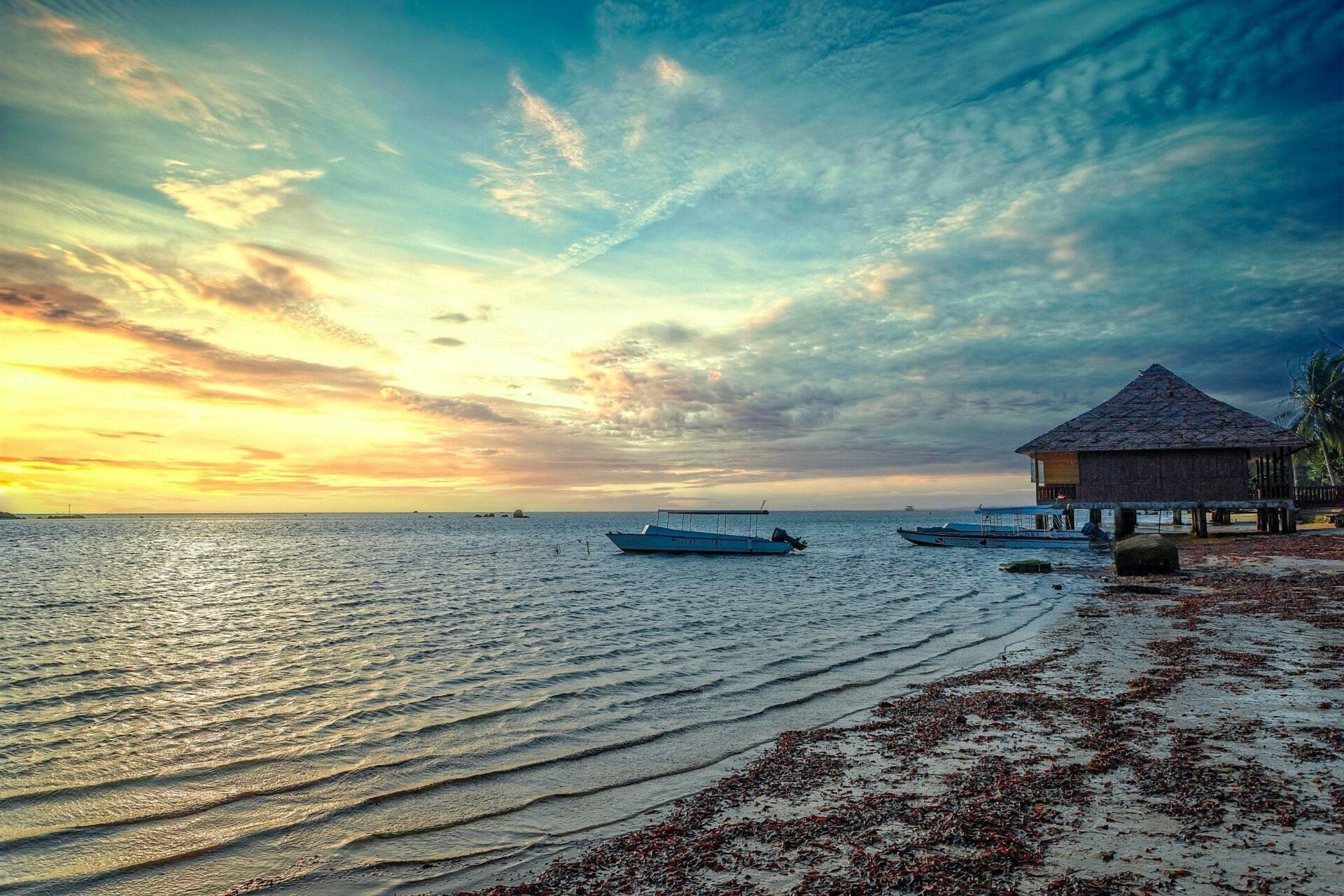 A tropical sunset over a sandy beach with a stilted bungalow and fishing boats at anchor