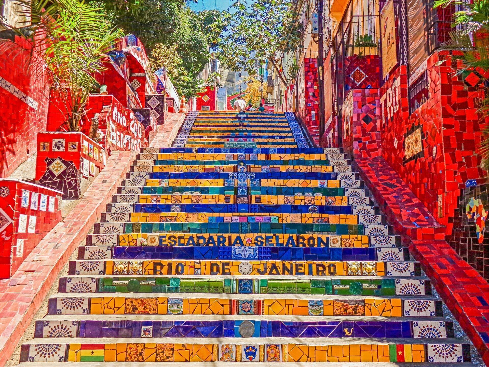 Escalier monumental aux marches colorées décorées de céramiques, entouré de murs rouges ornés, dans une ruelle pavée brésilienne