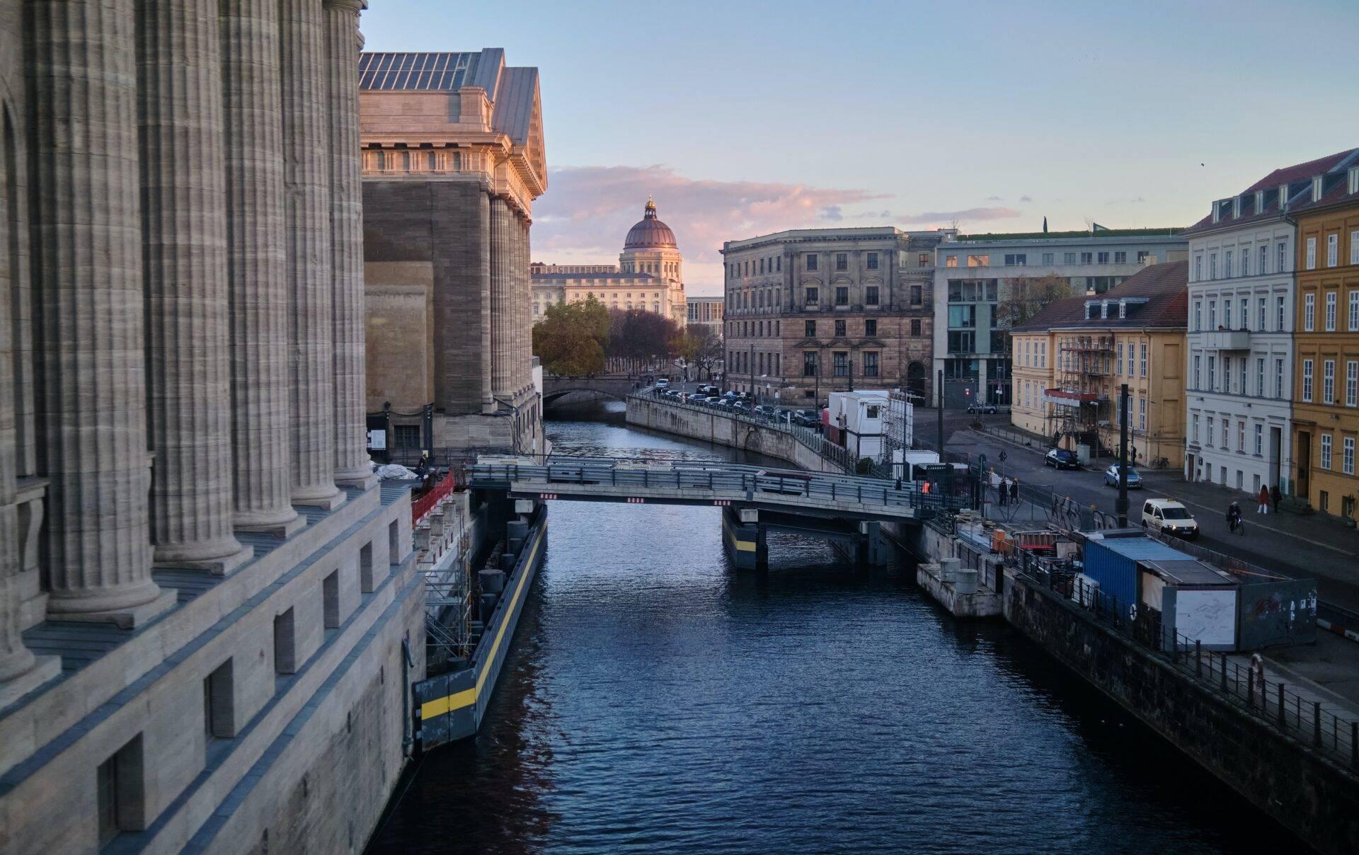 View along an urban canal with bridges, historic buildings and a grand architectural dome in the background