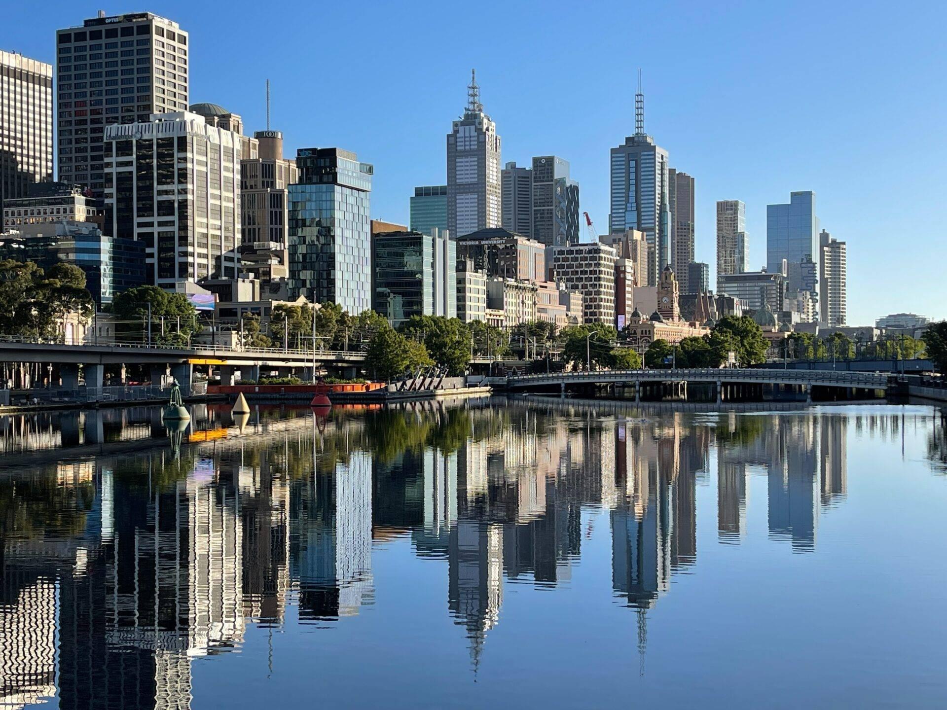 Skyline urbain moderne avec gratte-ciel reflétés dans les eaux calmes d’une rivière, arbres et quais au premier plan