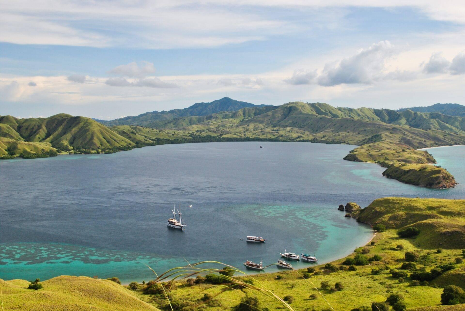Un lagon turquoise entouré de collines verdoyantes avec des bateaux traditionnels ancrés dans une baie tropicale