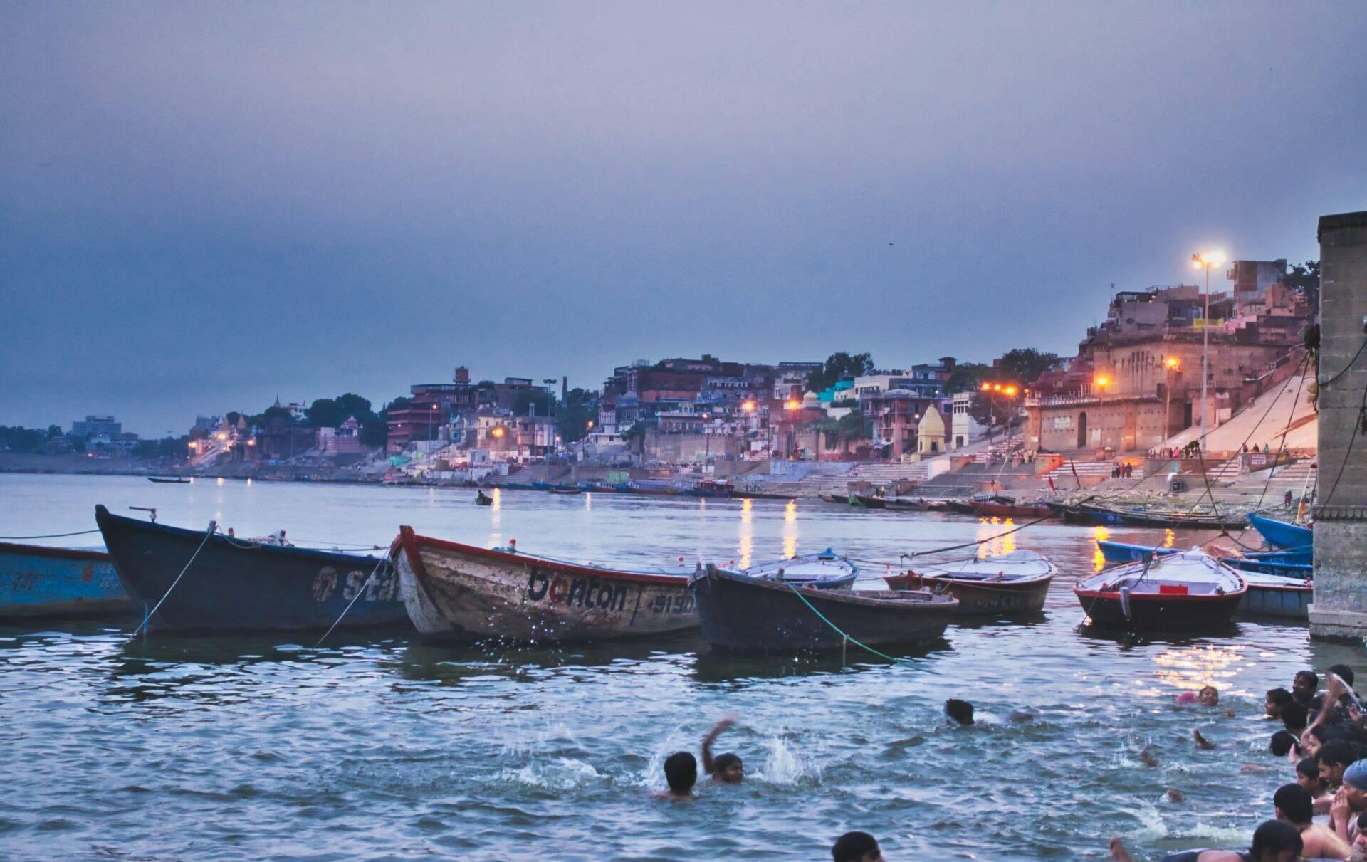 Colourful fishing boats moored in a bay at dusk, with temples and houses in the background