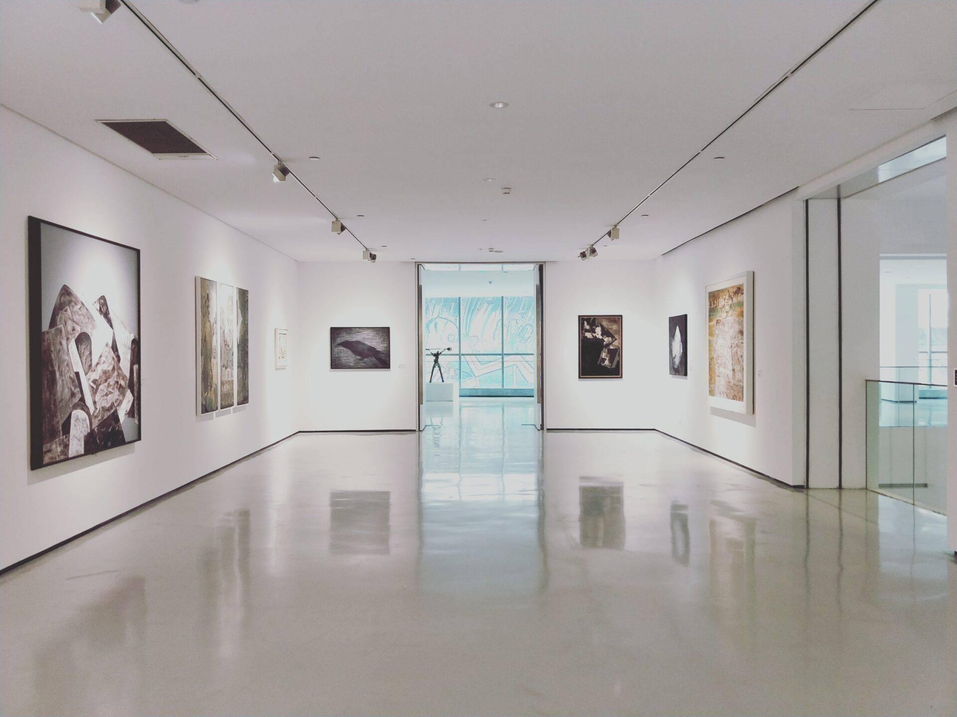Galerie d’art contemporain aux murs blancs avec tableaux exposés et baies vitrées donnant sur la mer