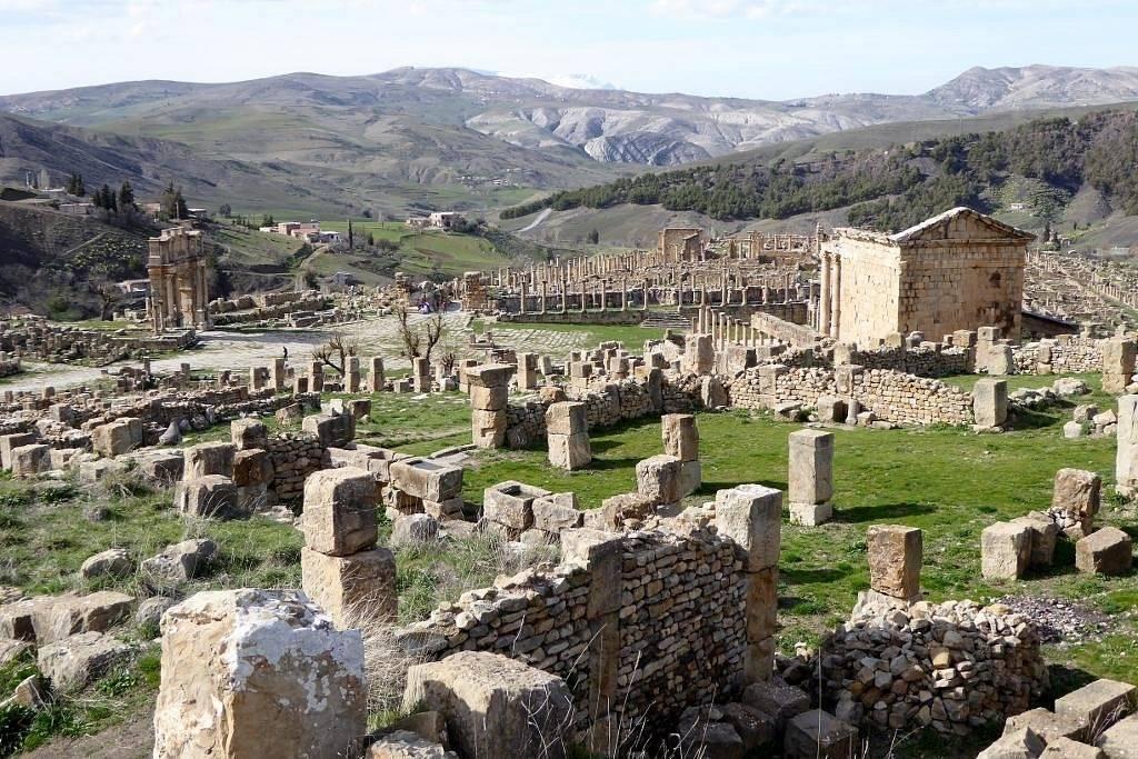 Ruines antiques avec colonnes de pierre dispersées dans un paysage vallonné montagneux verdoyant