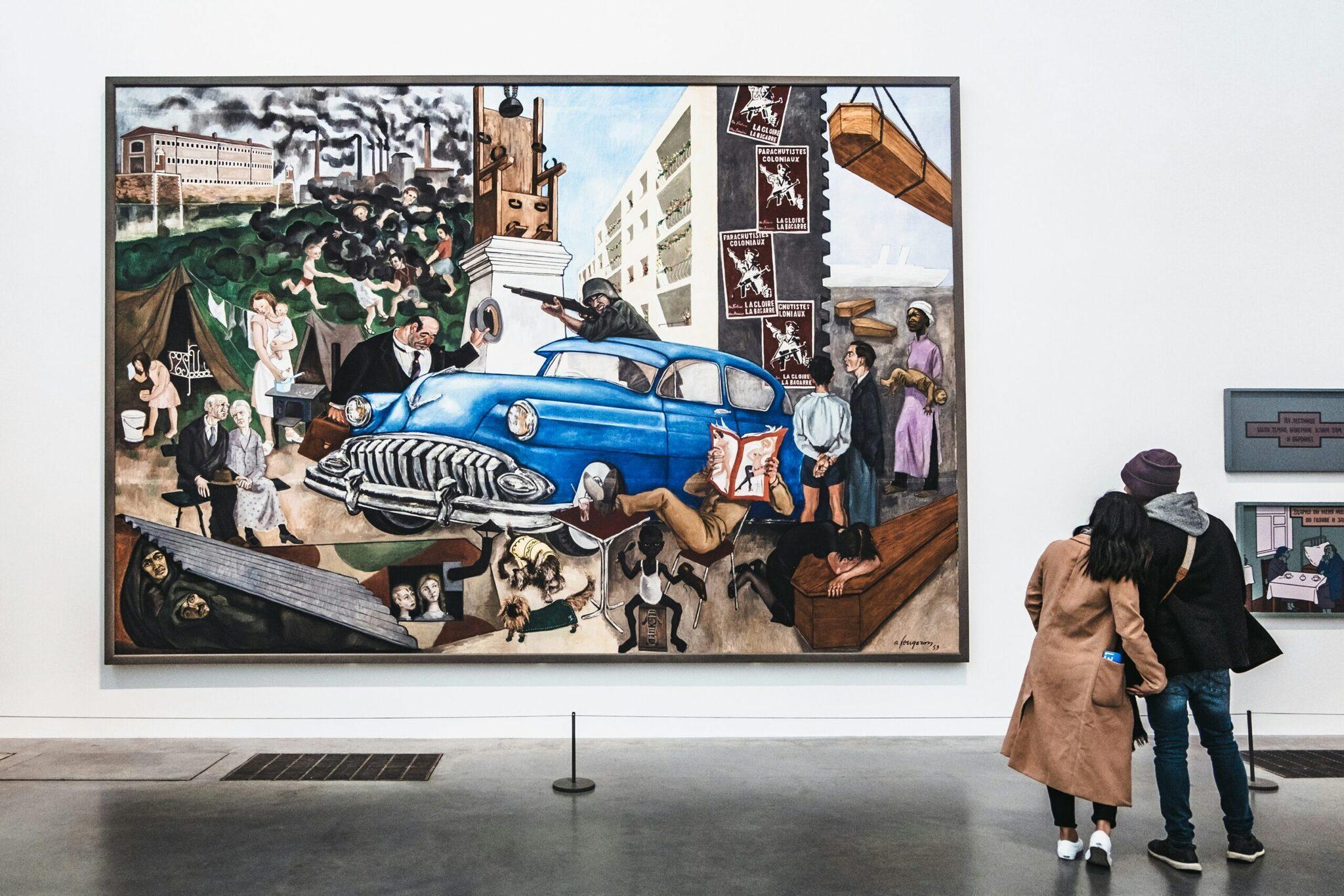Deux visiteurs observent une fresque murale colorée représentant une voiture bleue vintage et des scènes urbaines dans un musée