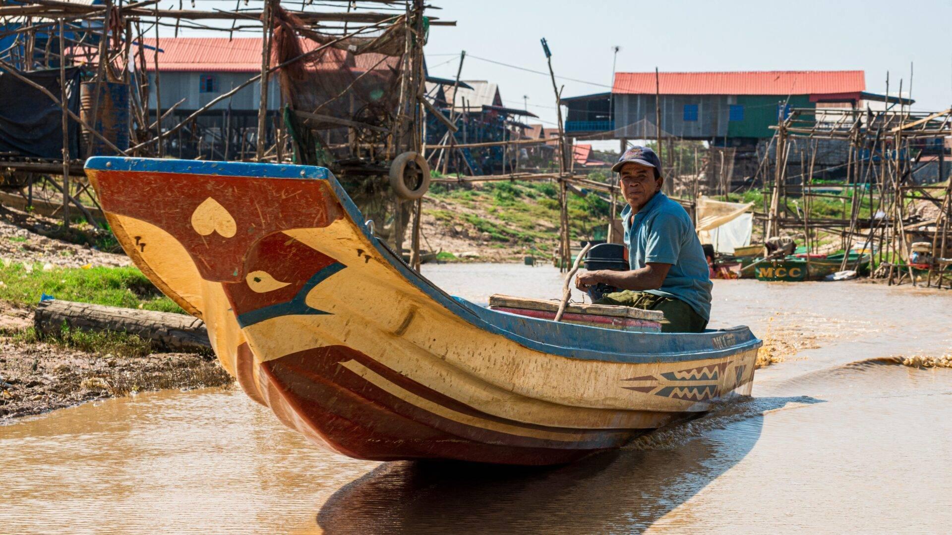 Un pêcheur dans une barque traditionnelle colorée décorée dans un village lacustre cambodgien avec des maisons sur pilotis
