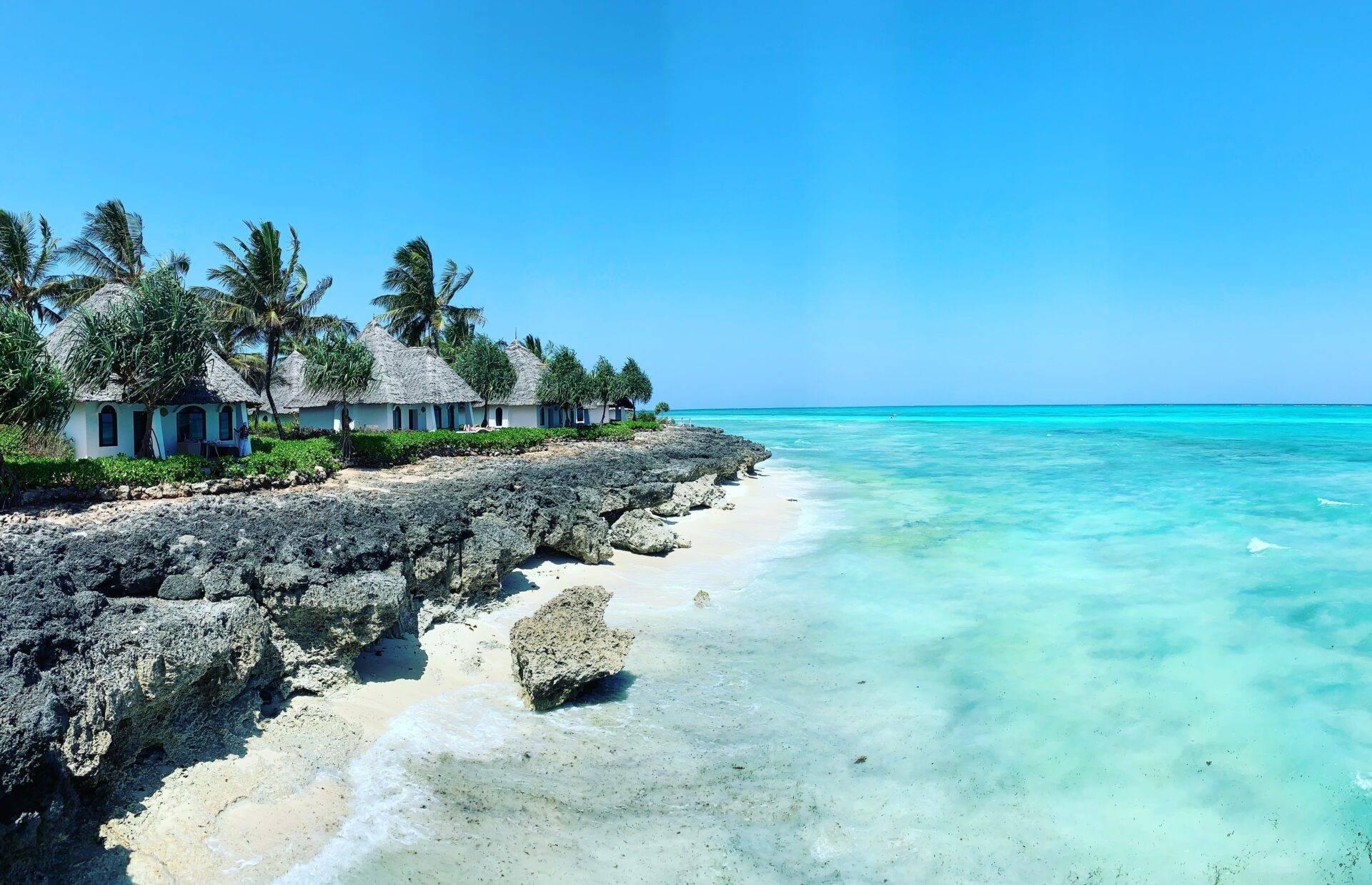 Small thatched-roof bungalows facing a turquoise lagoon and coral rocks in a tropical setting