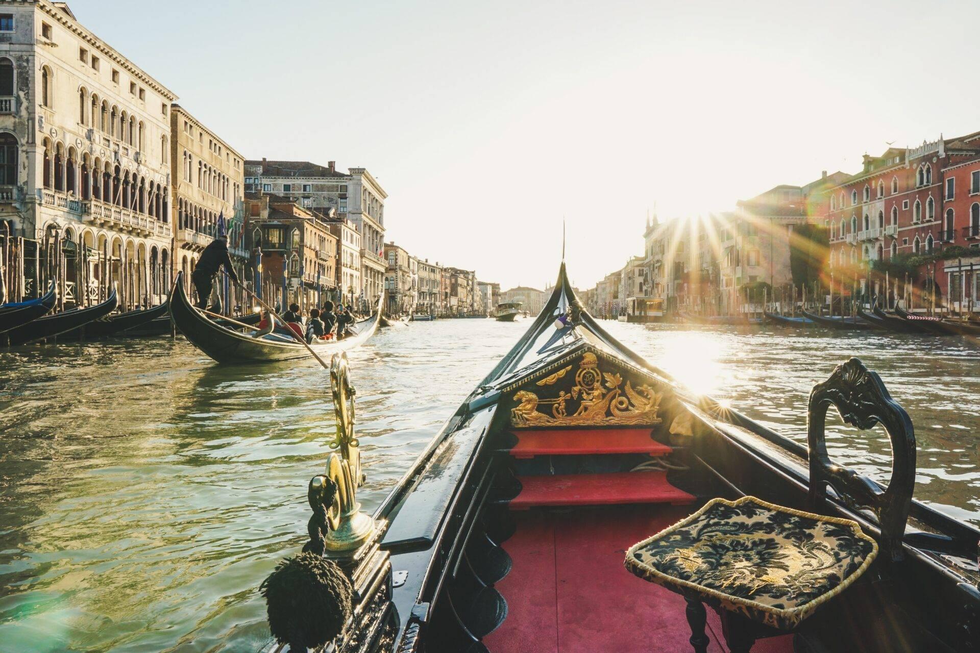 View from a decorated Venetian gondola navigating the Grand Canal with historic palaces and sunlight