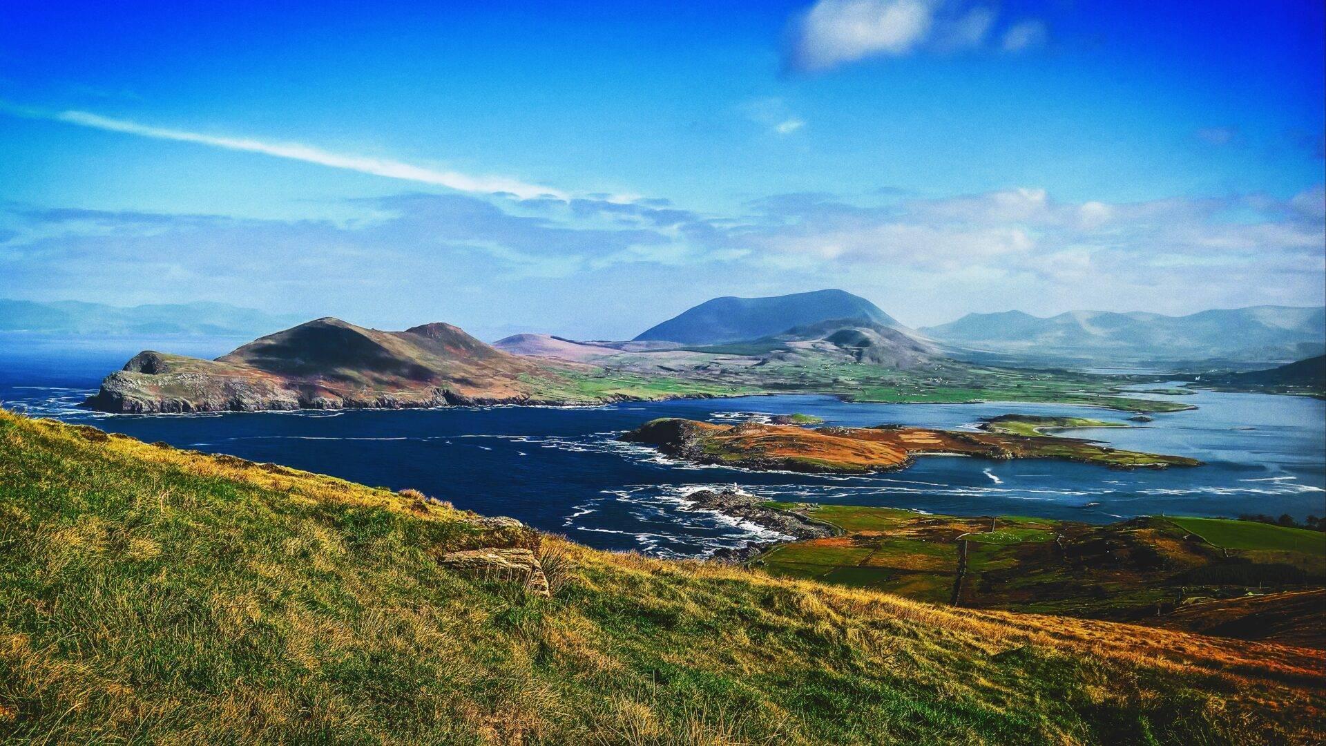 Irish coastal scenery with volcanic islands, green mountains and a blue bay under clear skies