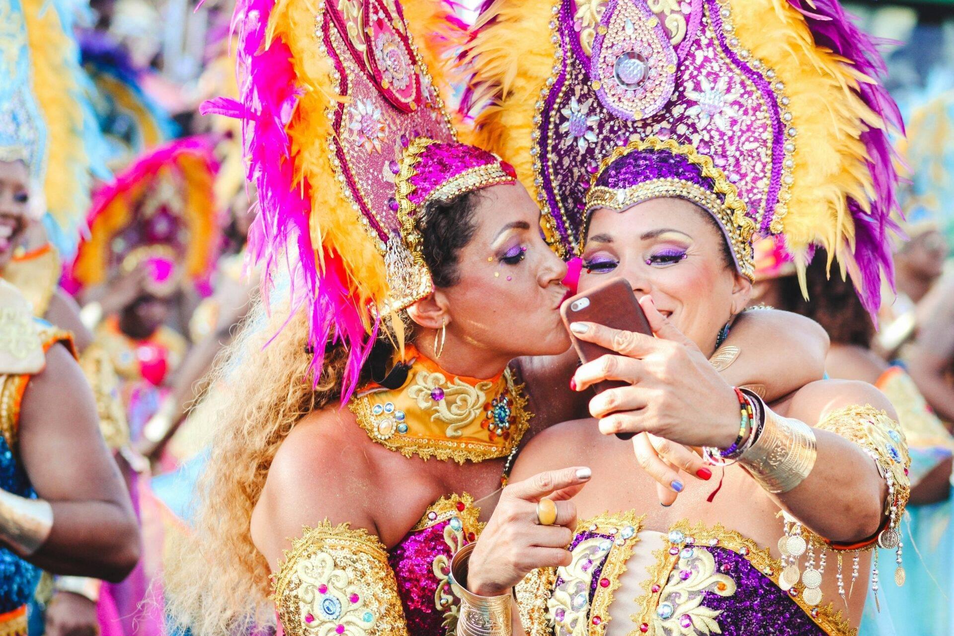 Deux danseuses en costumes colorés et plumed participent à un carnaval tropical, l’une prenant un selfie