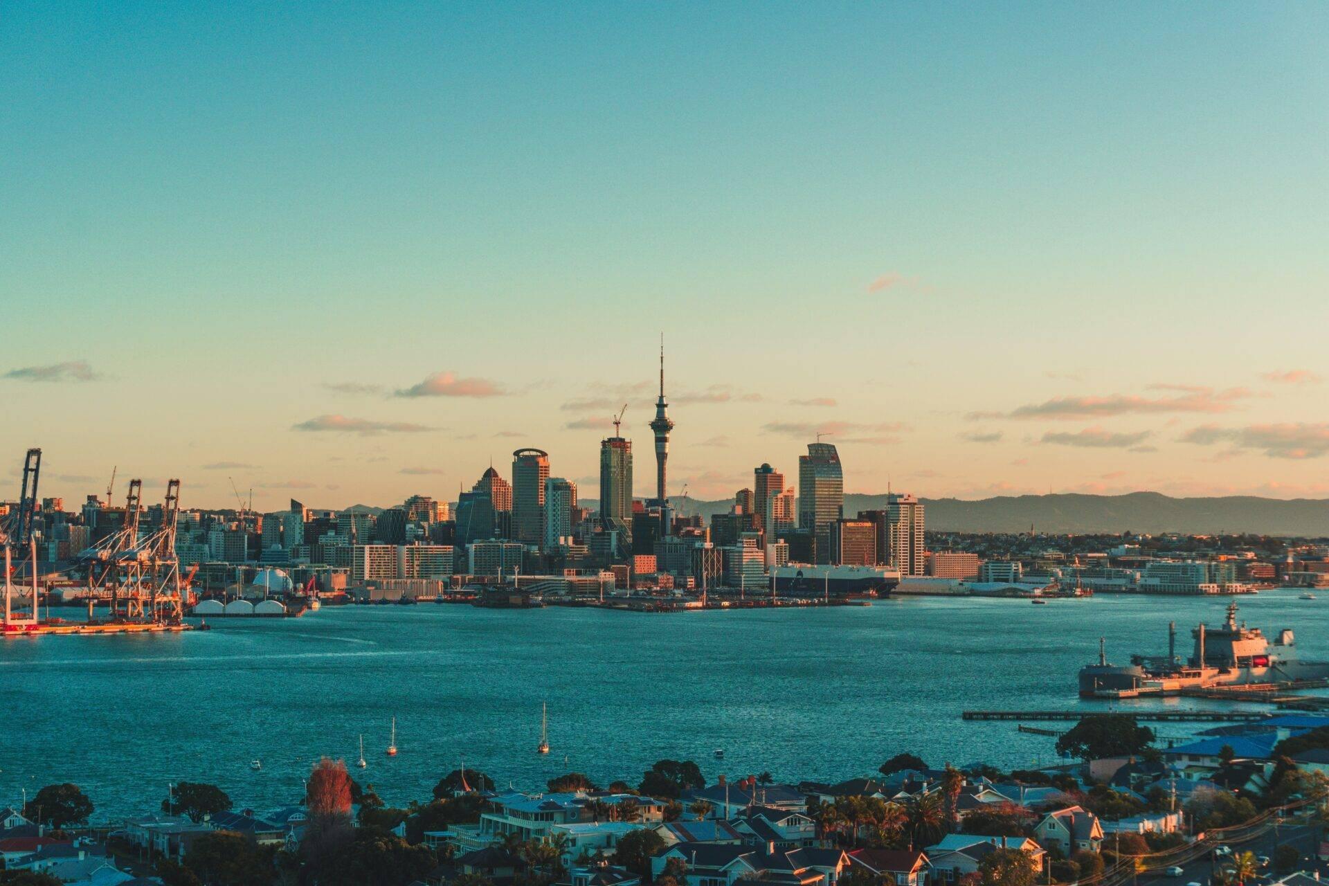 Vue panoramique d’une skyline urbaine côtière avec gratte-ciels, port maritime animé et résidences en premier plan au coucher du soleil