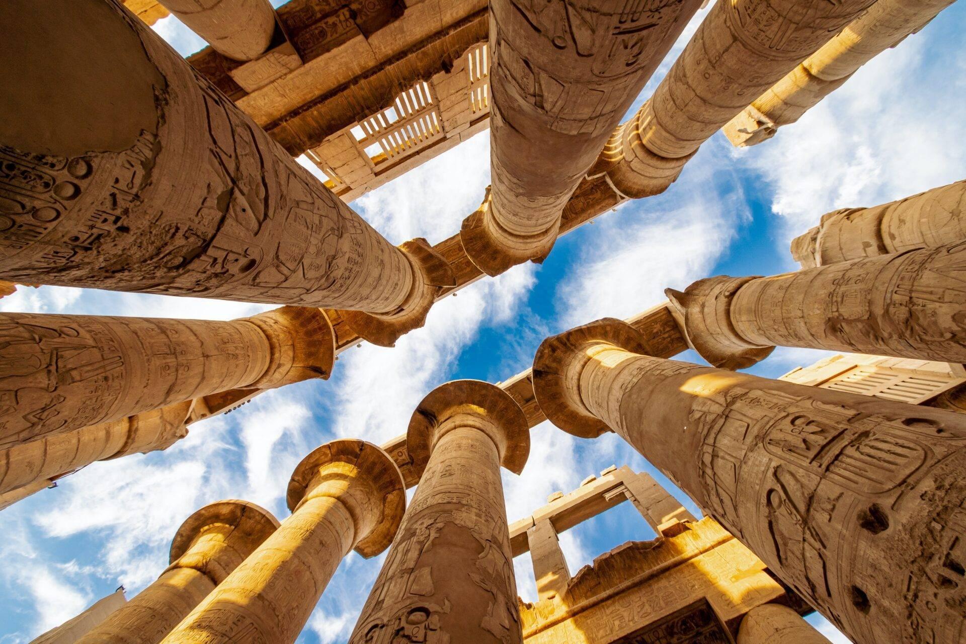 Looking up at pharaonic columns covered in hieroglyphs inside an ancient Egyptian temple