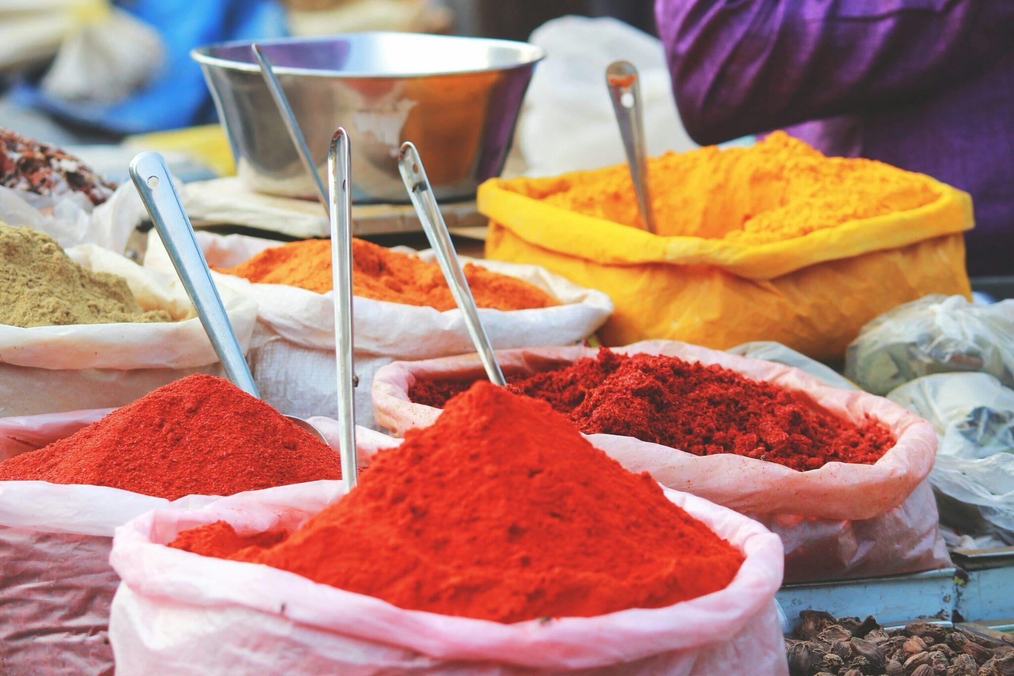 Étal de marché coloré avec épices en poudre rouge et orange dans des bols roses et sacs jaunes