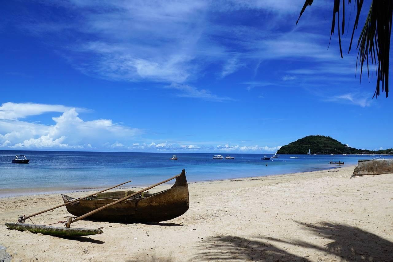 A traditional wooden boat beached on white sand in front of a turquoise bay with a wooded island beyond
