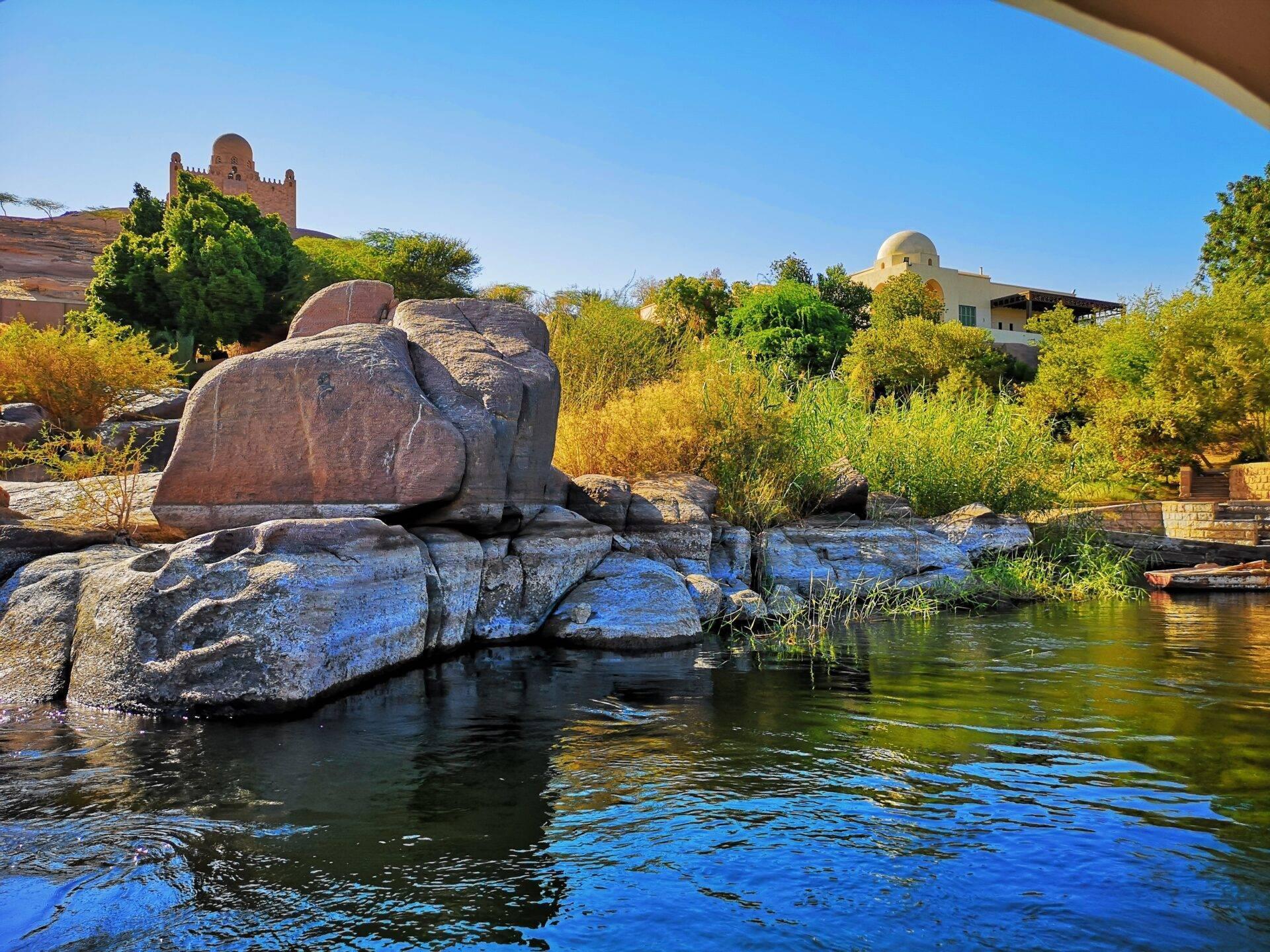 View over the Nile with granite rocks, a mosque and traditional buildings in the background