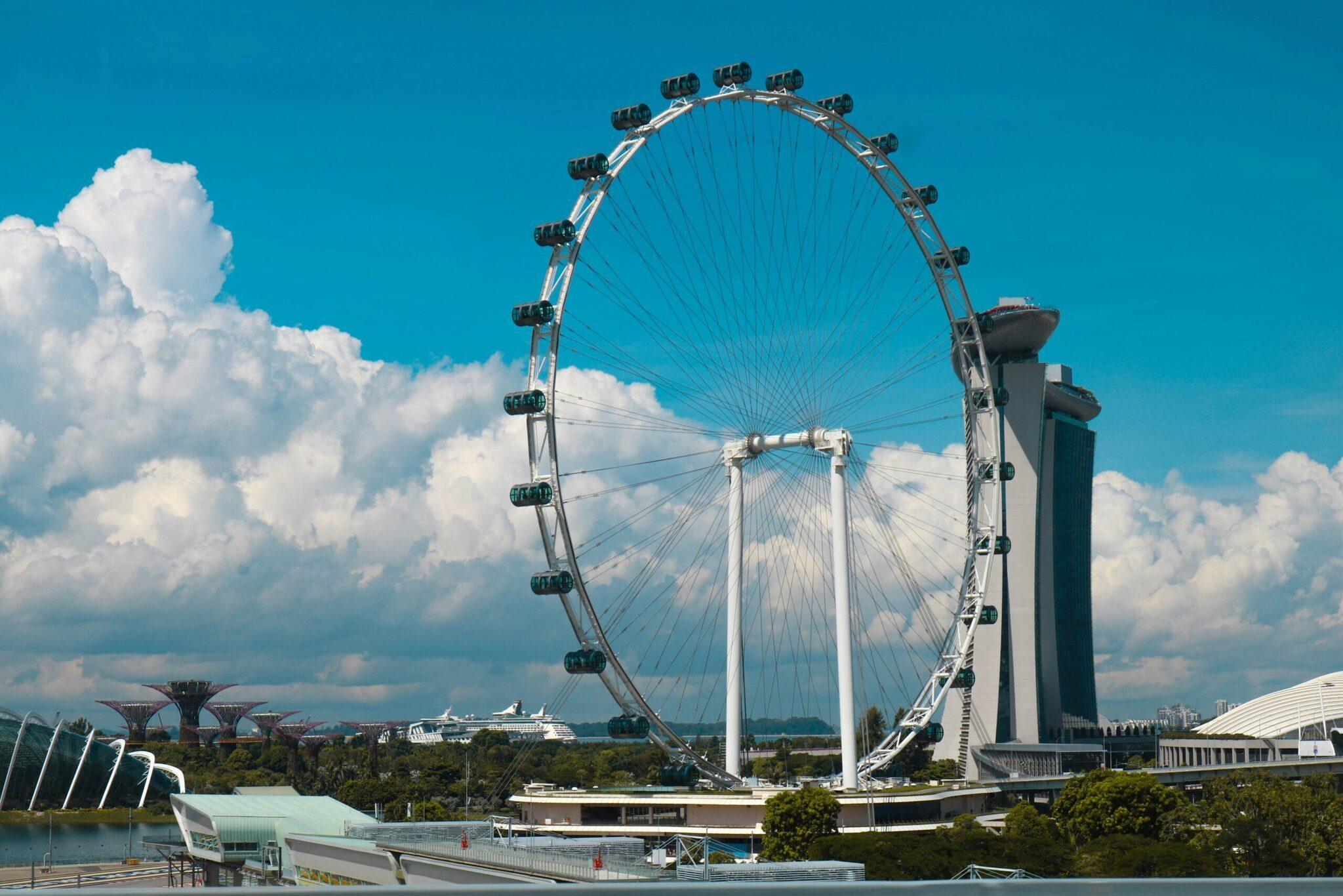 Une grande roue futuriste blanche avec des cabines noires domine le paysage urbain sous un ciel bleu dégagé