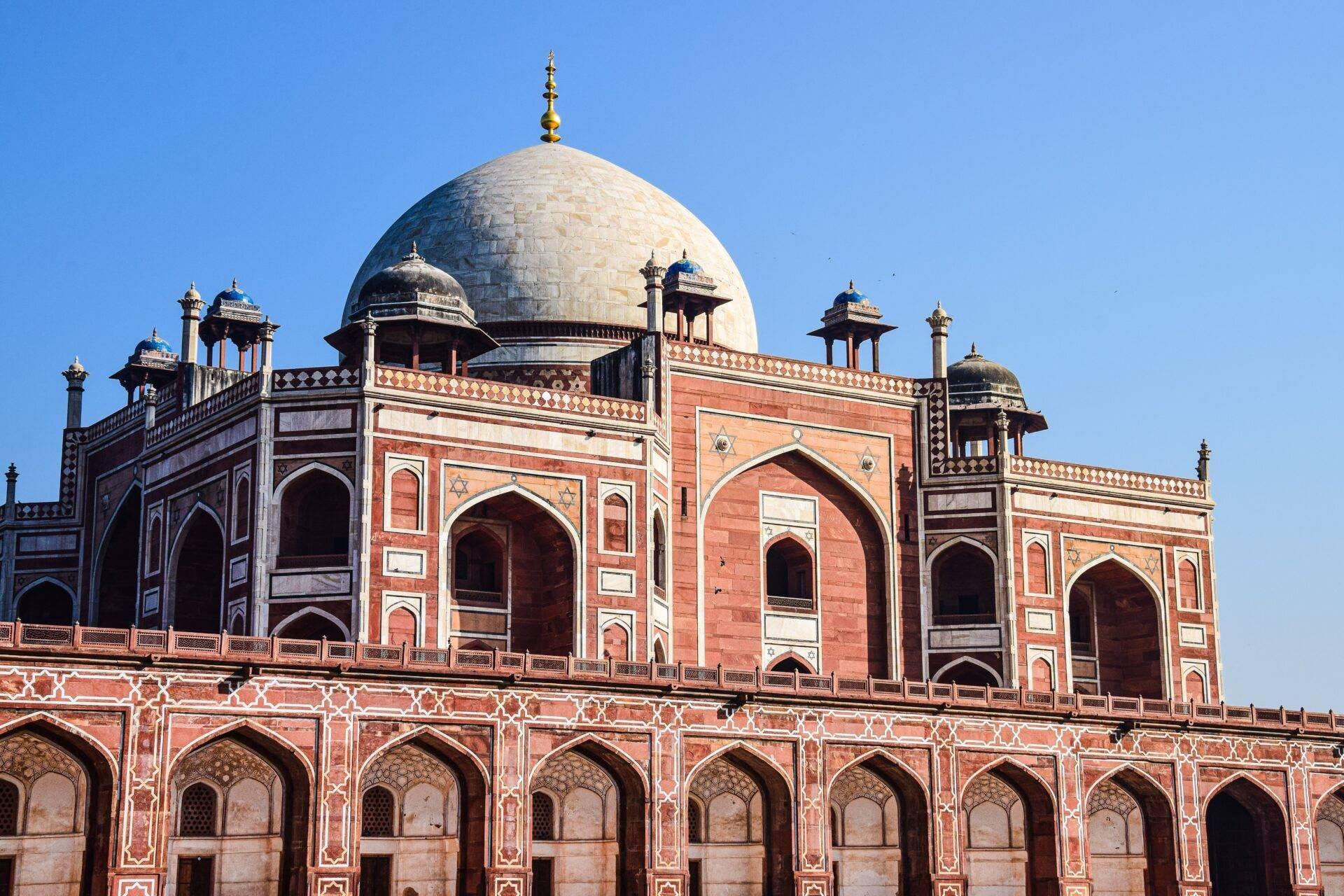 Imposing mausoleum in red sandstone and white marble with a white dome and golden ornaments under a clear blue sky