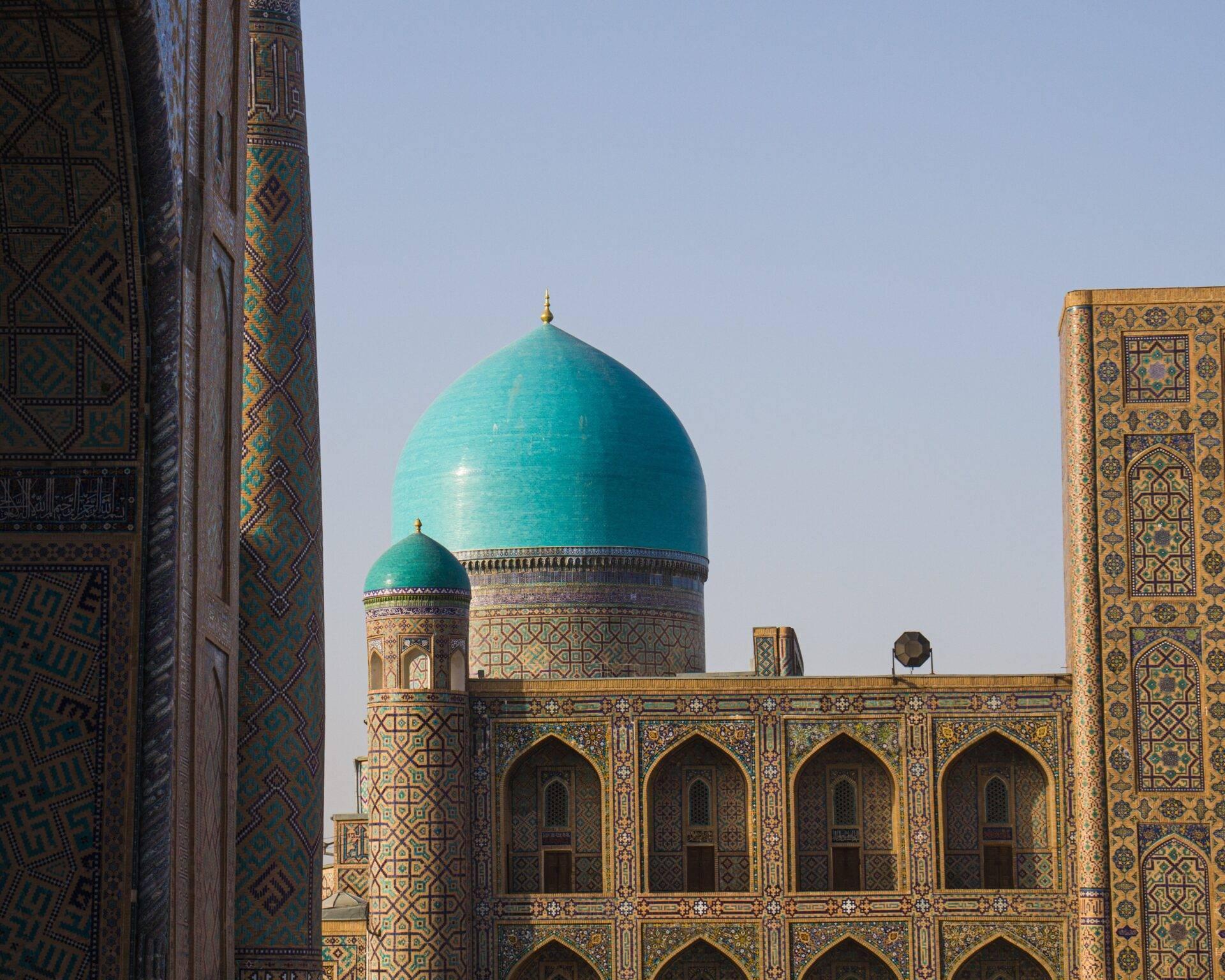 Islamic mausoleum decorated with turquoise and gold, featuring ornate minarets and a blue ribbed dome