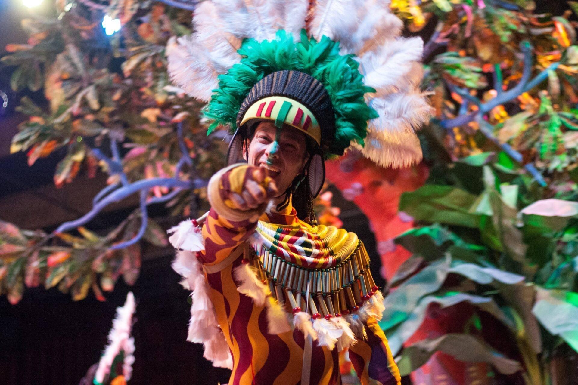 A dancer in a colourful traditional costume with a green feathered headdress at a Brazilian festive parade