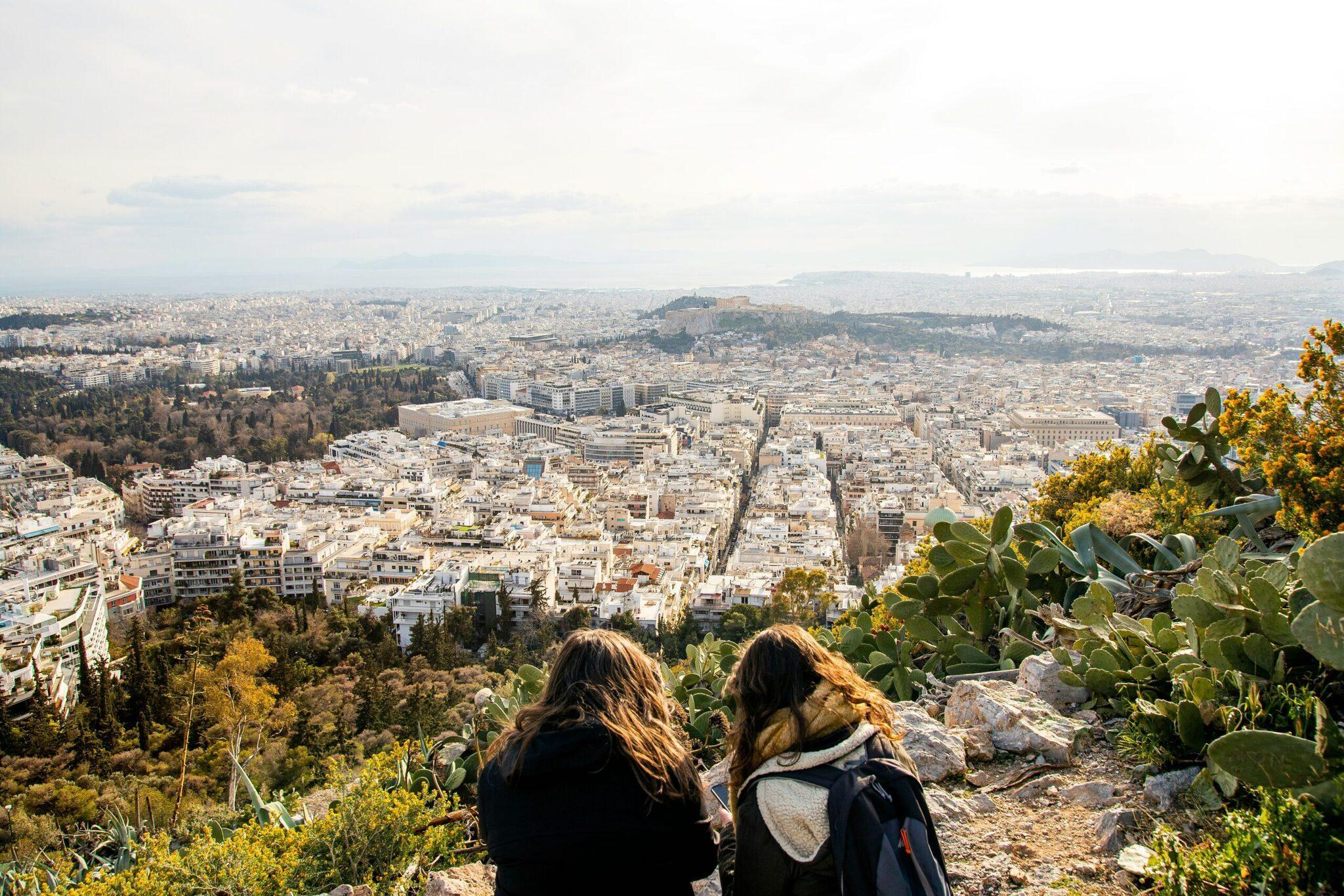 Deux femmes admirent la vue panoramique sur une ville méditerranéenne depuis un point culminant avec végétation locale
