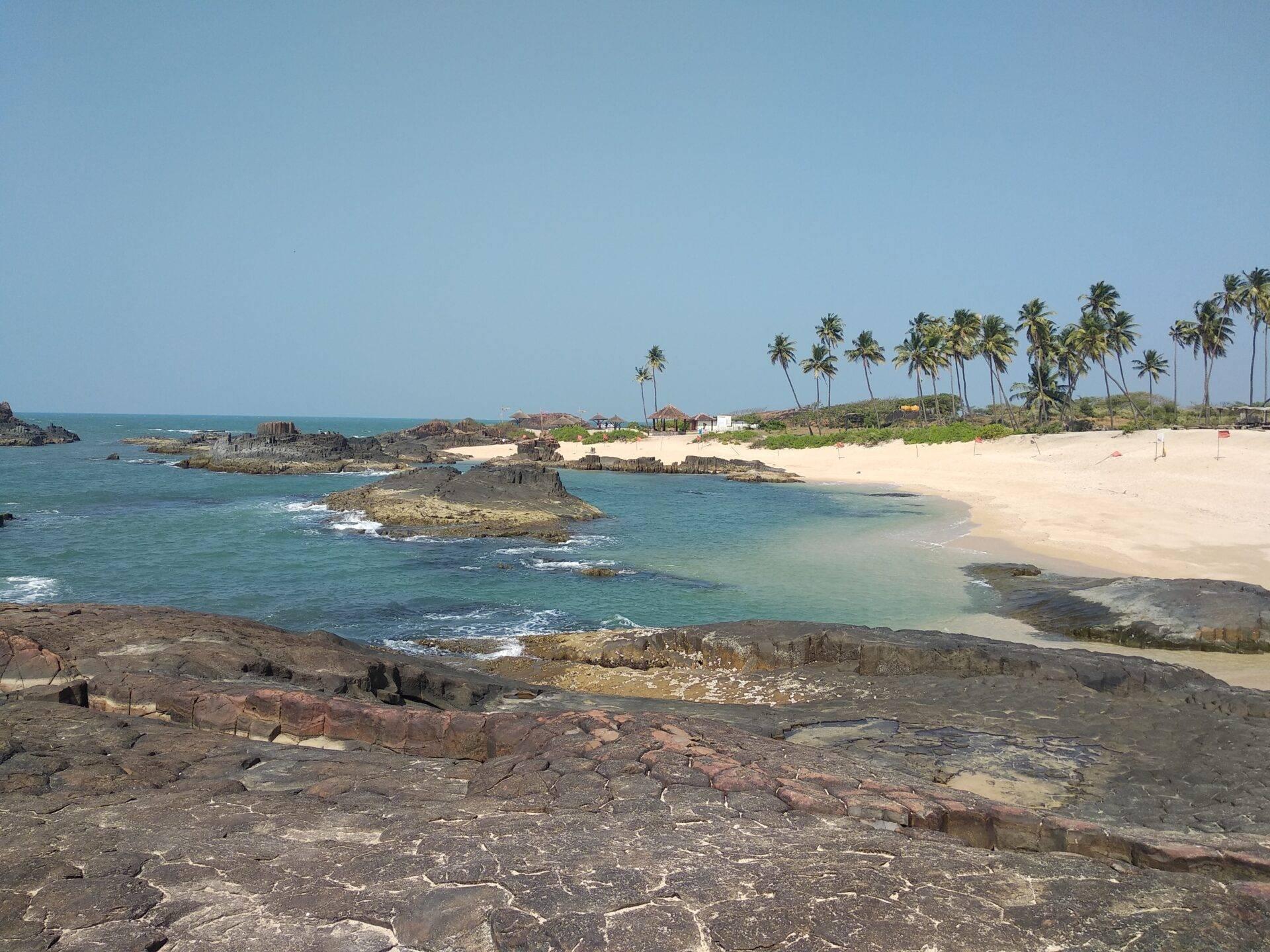Coastal view with white sandy beach, volcanic rocks, coconut palms and small rocky islets in turquoise water