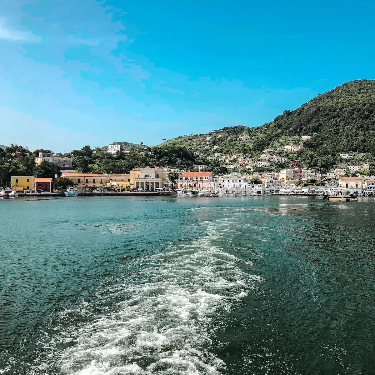 Vue depuis la mer d’un village côtier méditerranéen coloré avec maisons pastel et collines boisées
