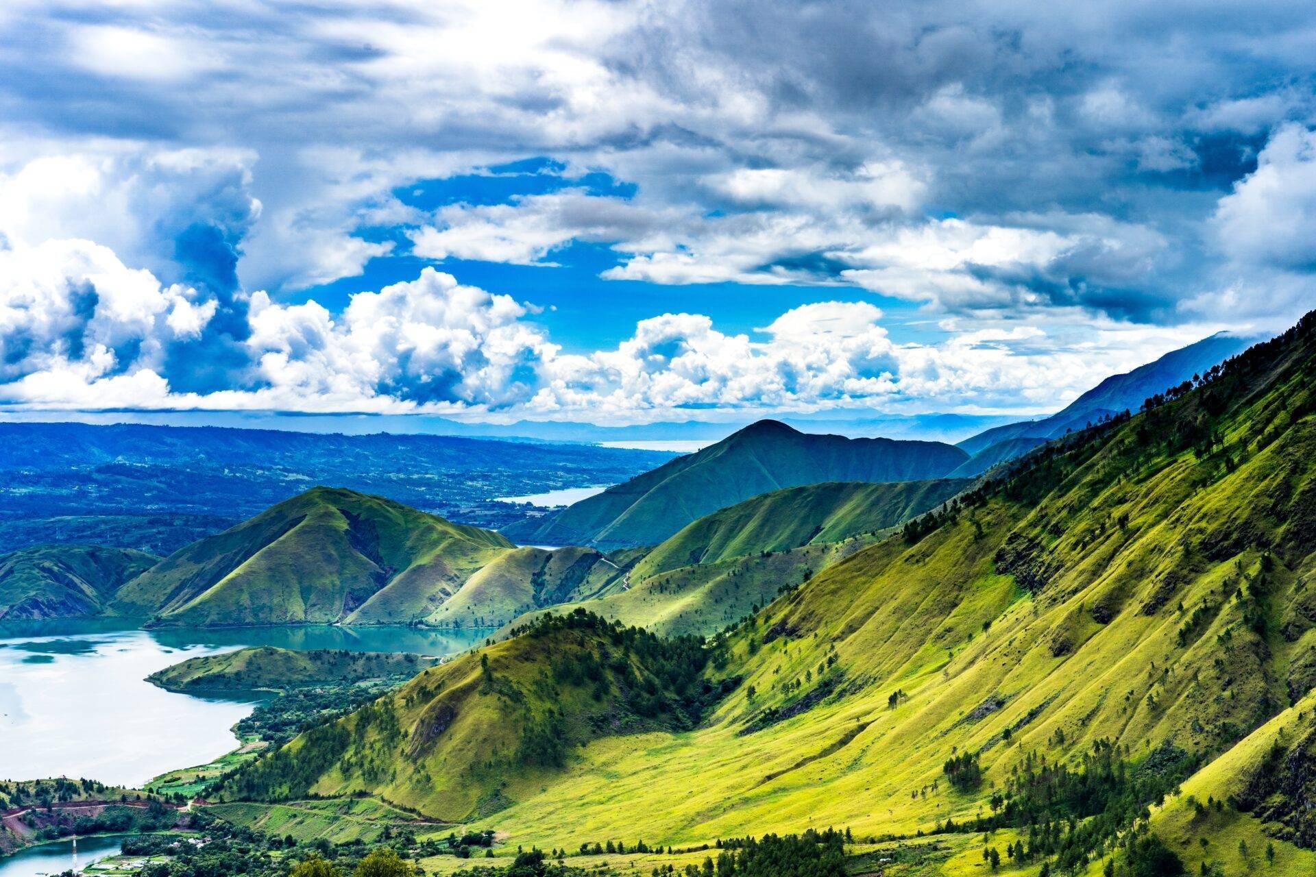 Paysage montagneux tropical avec lacs, forêts verdoyantes et ciel nuageux bleu, illustrant la beauté naturelle volcanique