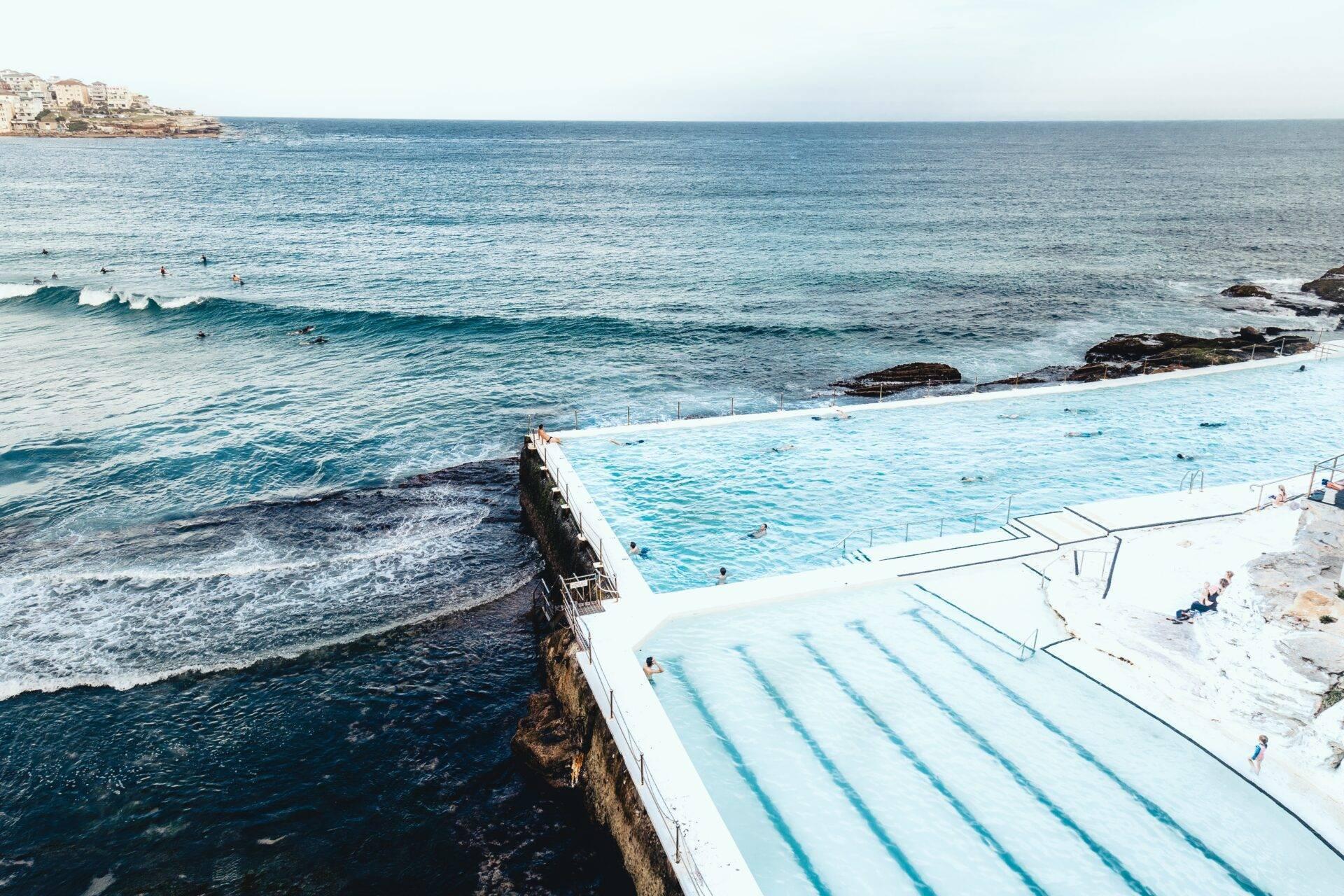 Piscine olympique en bord de mer avec vue sur l’océan turquoise et côte rocheuse sous ciel dégagé