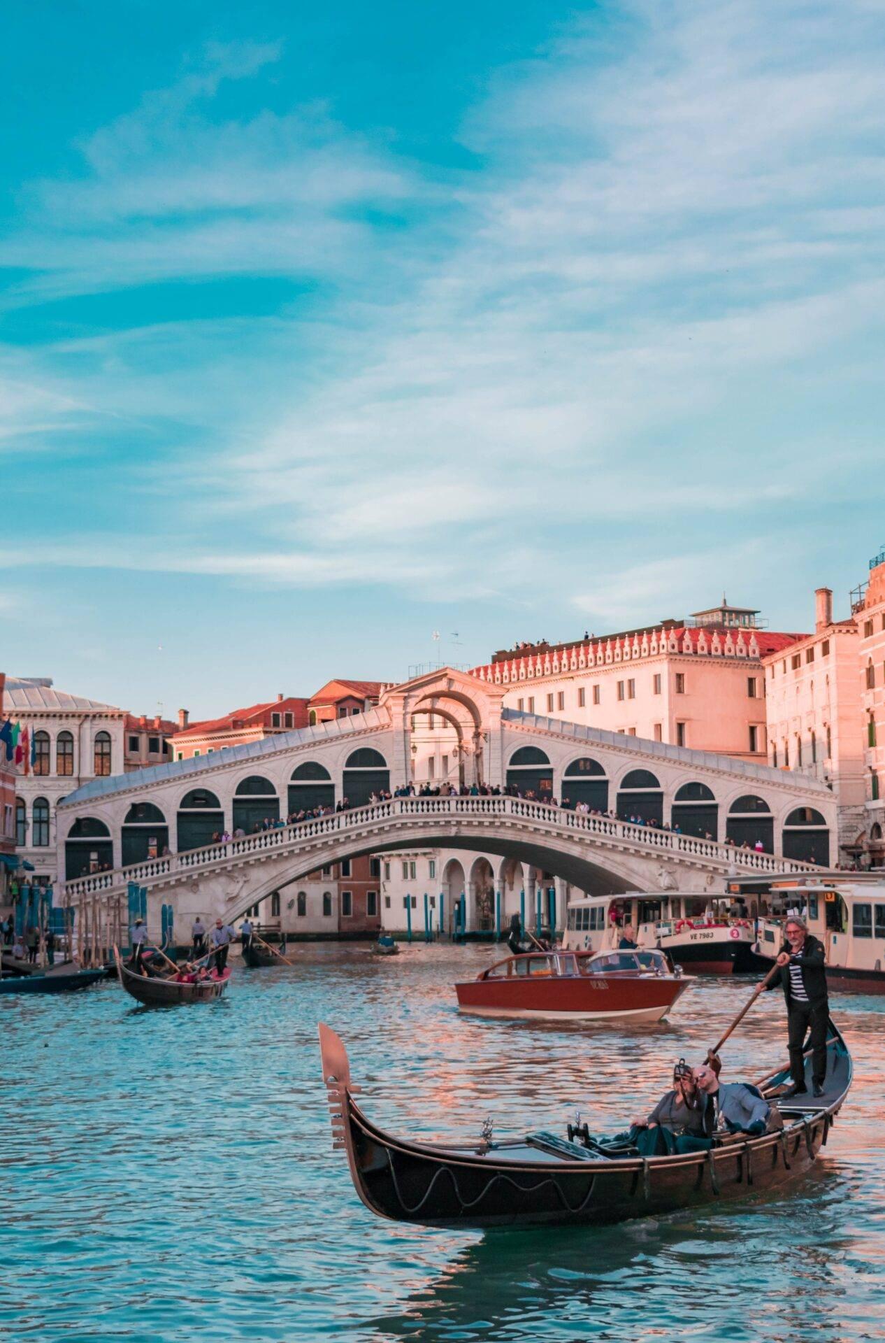 Gondolas and visitors on the Grand Canal in front of the Rialto Bridge with its pink facades and typical Venetian architecture