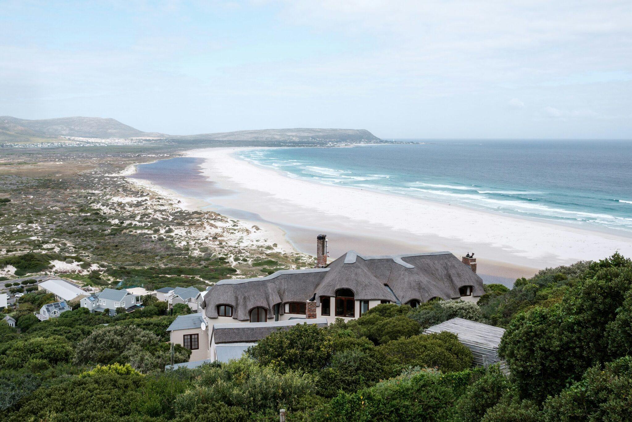 A modern thatched-roof house overlooking a vast white-sand beach and turquoise ocean in South Africa