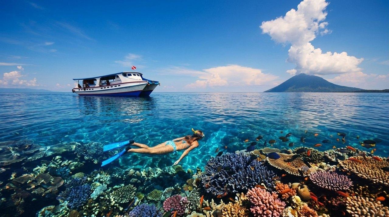 A freediver explores a colourful coral reef near a boat, with a volcano visible in the background