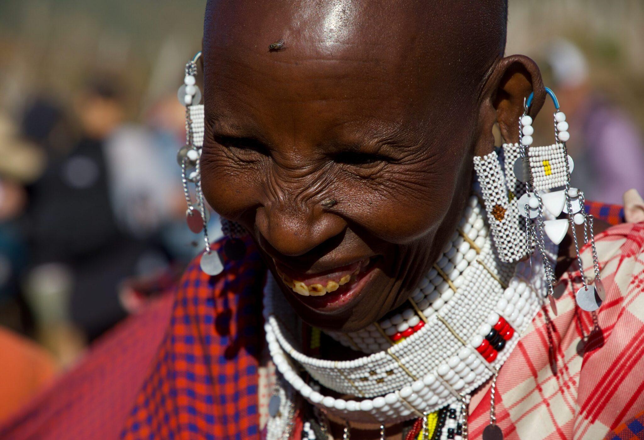 Femme souriante portant des vêtements traditionnels colorés et des bijoux perlés blancs caractéristiques de la culture africaine