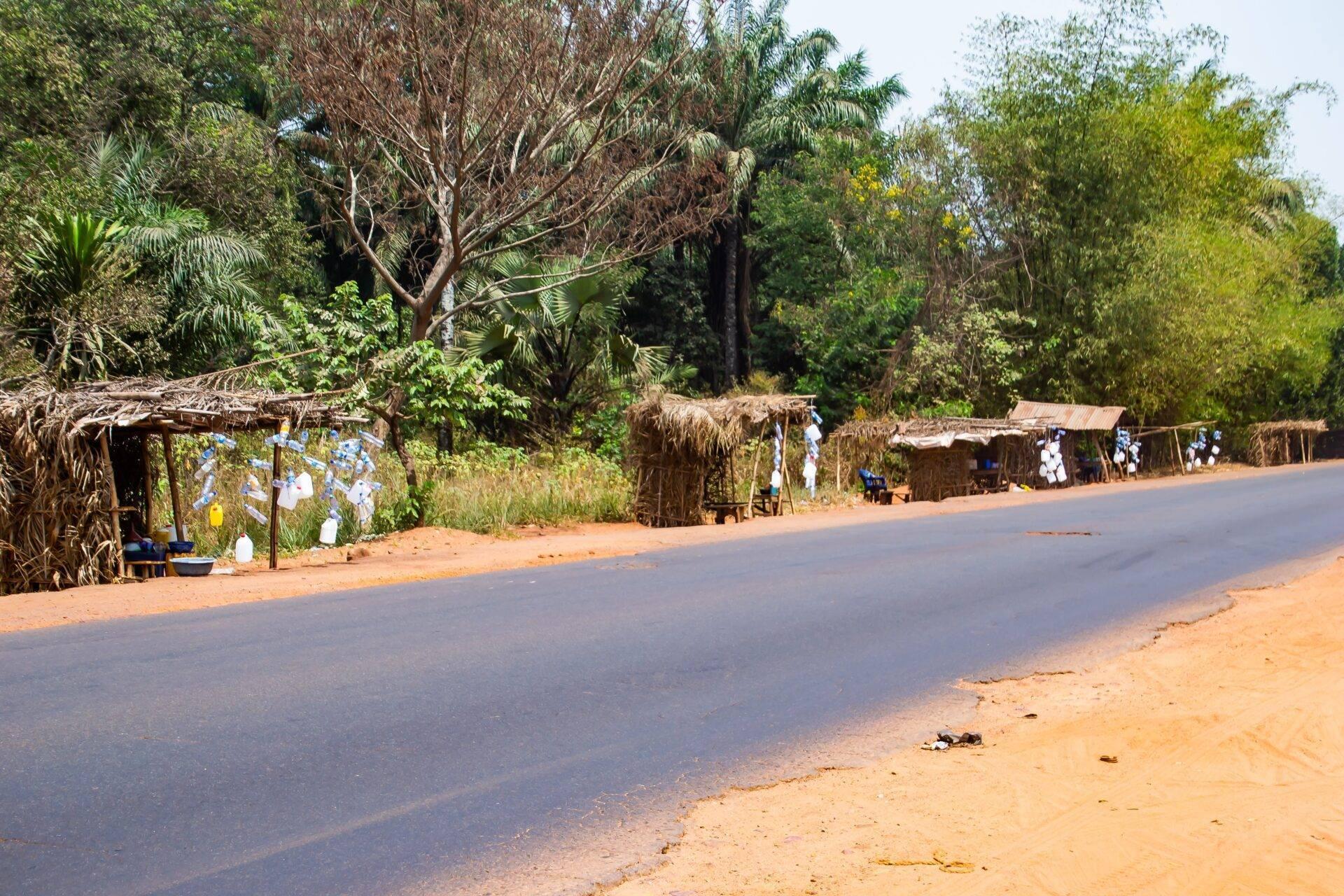 Une route pavée traversant un village avec des habitations en paille traditionnelles et une végétation tropicale dense