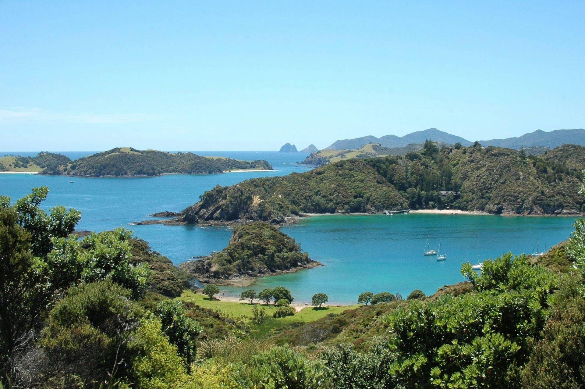 Vue panoramique d’une baie côtière avec îles boisées, plages turquoise et voiliers ancrés dans une eau cristalline