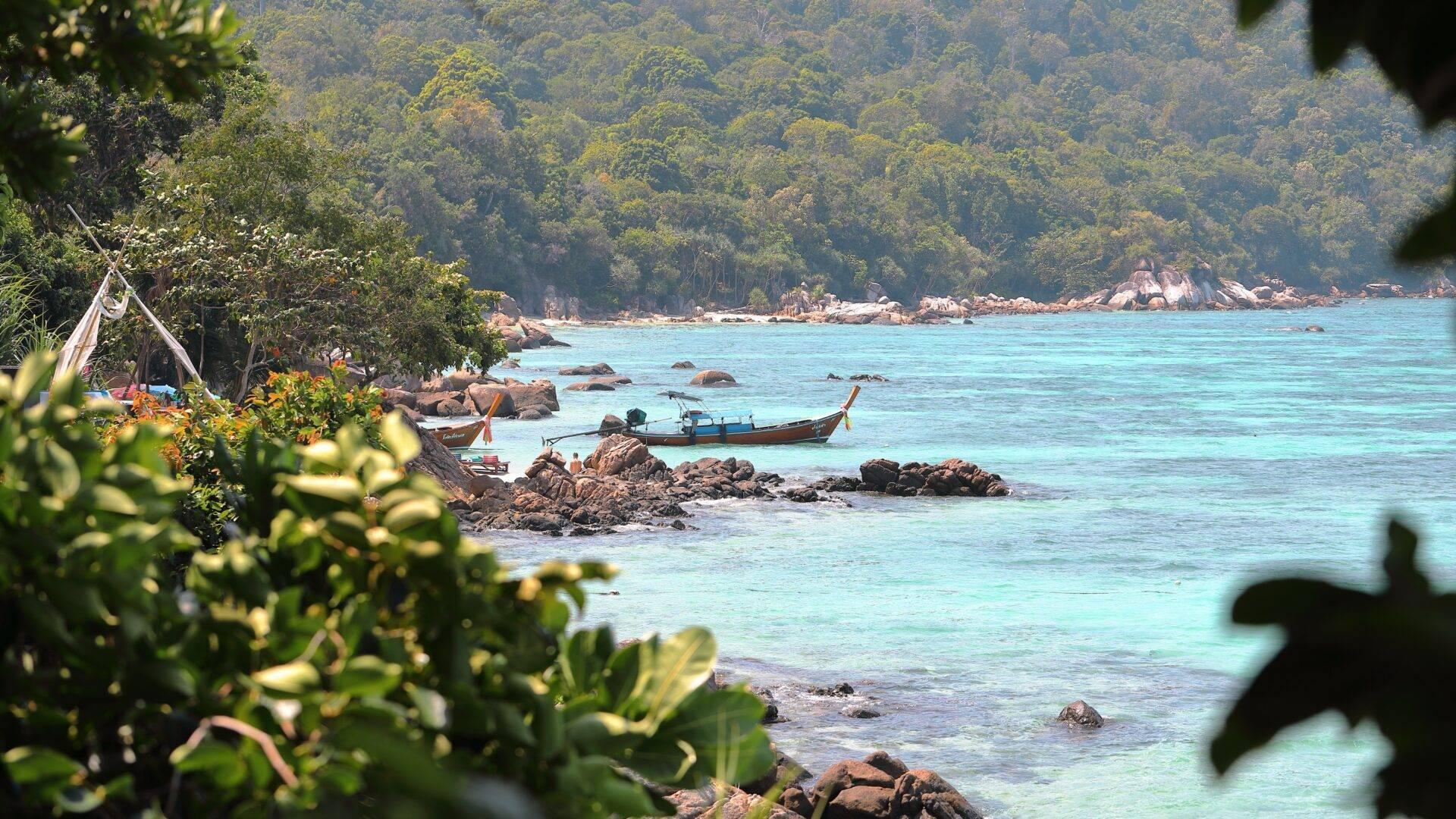Vue côtière tropical avec bateau à longue queue, eaux turquoise, rochers et dense jungle en arrière-plan