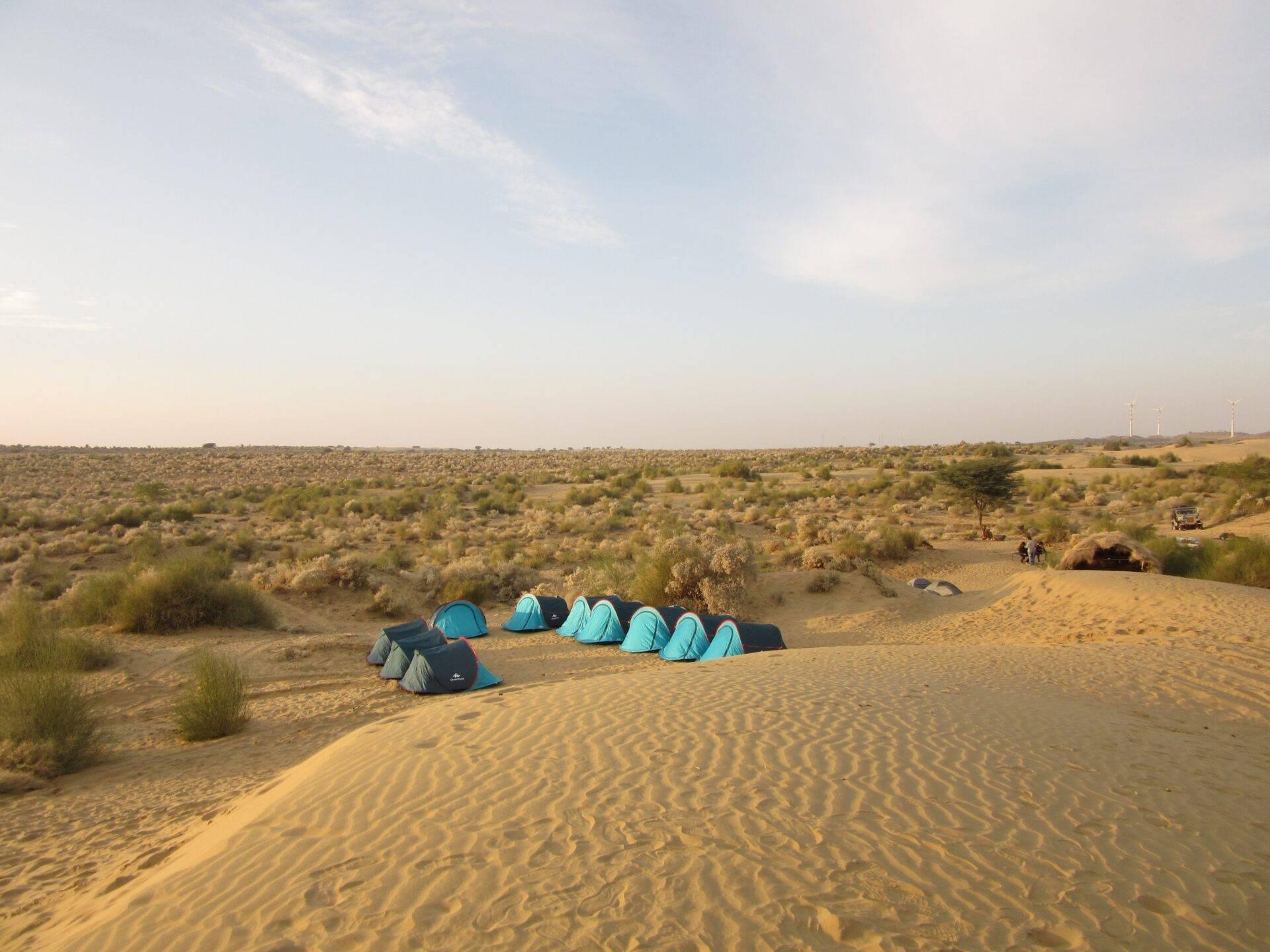 Blue tent camp in the Rajasthan desert with sand dunes and sparse vegetation