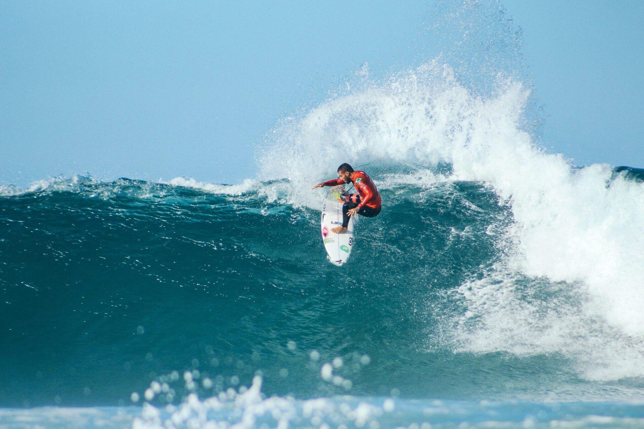 A surfer in a red wetsuit riding a powerful wave under a clear blue sky
