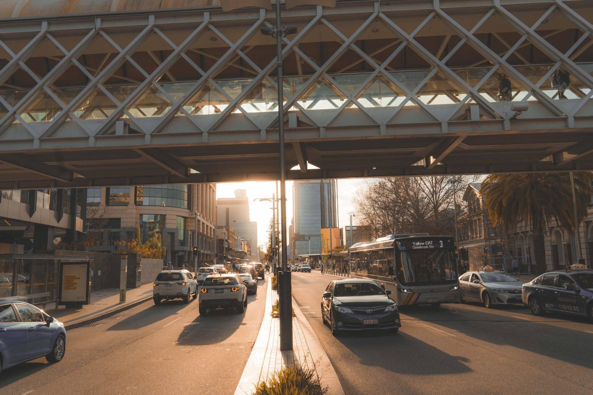 Une rue urbaine australienne sous une structure de verre avec voitures, bus et bâtiments modernes au coucher de soleil
